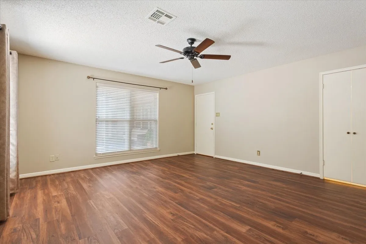 Spacious primary bedroom room featuring warm wood-like vinyl flooring, ceiling fan, and natural light from multiple windows