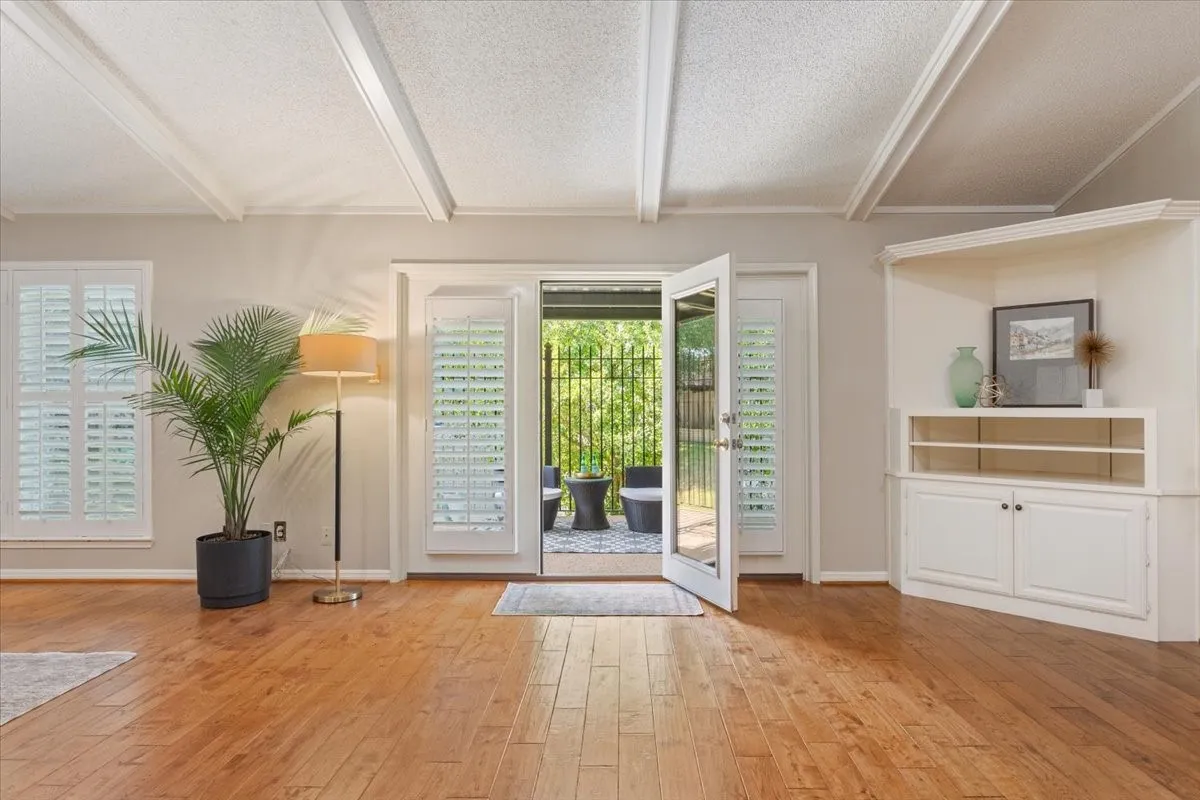 Spacious open-concept living area that opens to a covered back patio featuring coffered ceiling with recessed lighting, hardwood flooring throughout, and a custom built-in