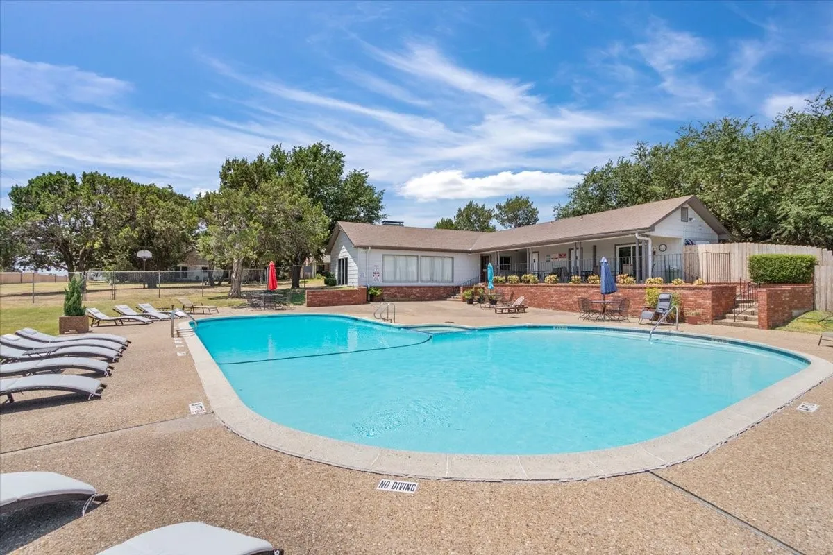 Community pool -Resort-style swimming pool featuring crystal-clear waters, curved design with integrated shallow lounging area, and surrounding concrete decking with lounge seating