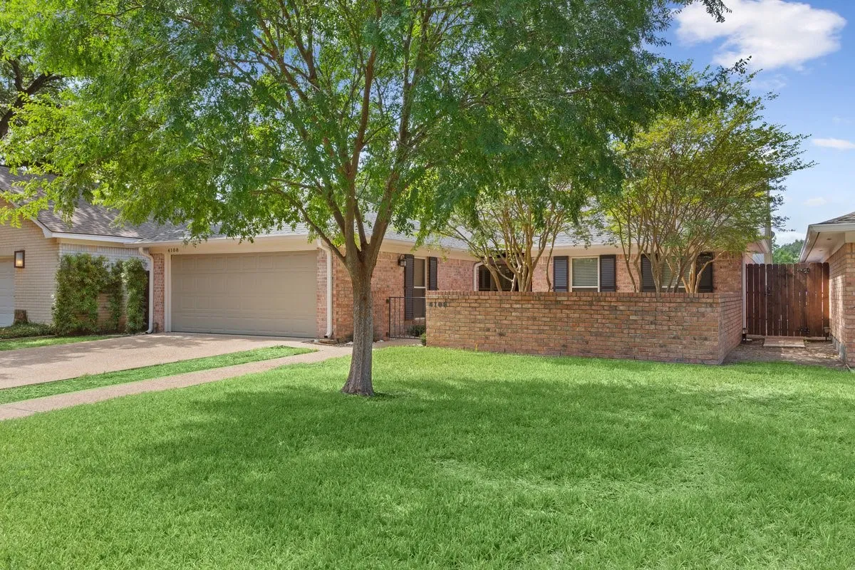Expansive front lawn with a mature Chinese Elm tree, brick exterior, and a two-car garage
