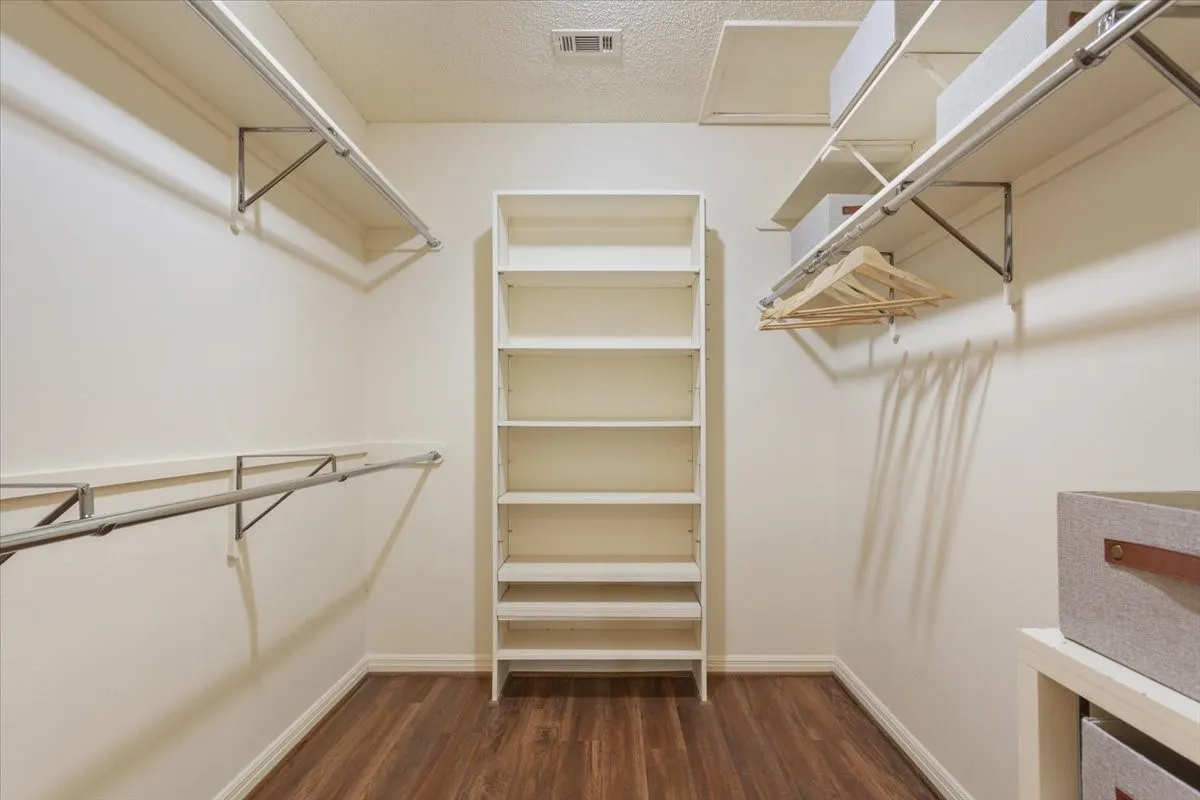 Walk-in closet off of primary bathroom featuring vinyl flooring, built-in shelving, and hanging rods