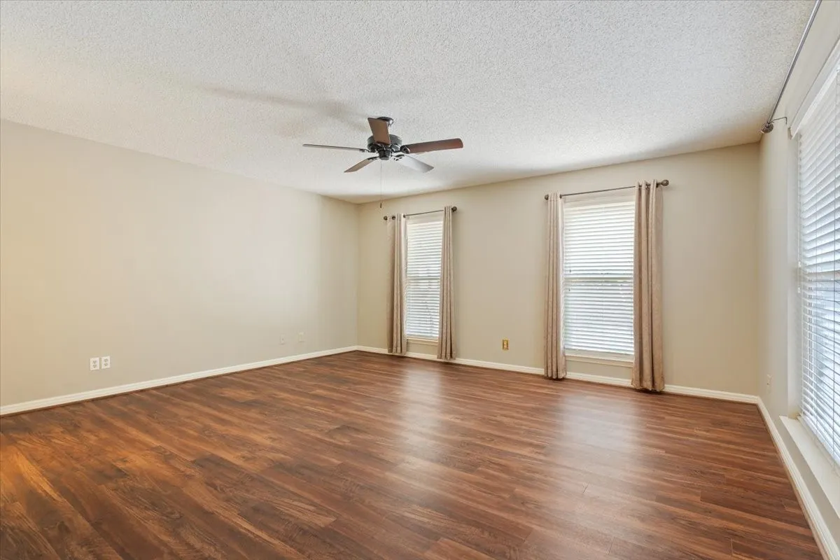 Spacious primary bedroom room featuring warm wood-like vinyl flooring, ceiling fan, and natural light from multiple windows