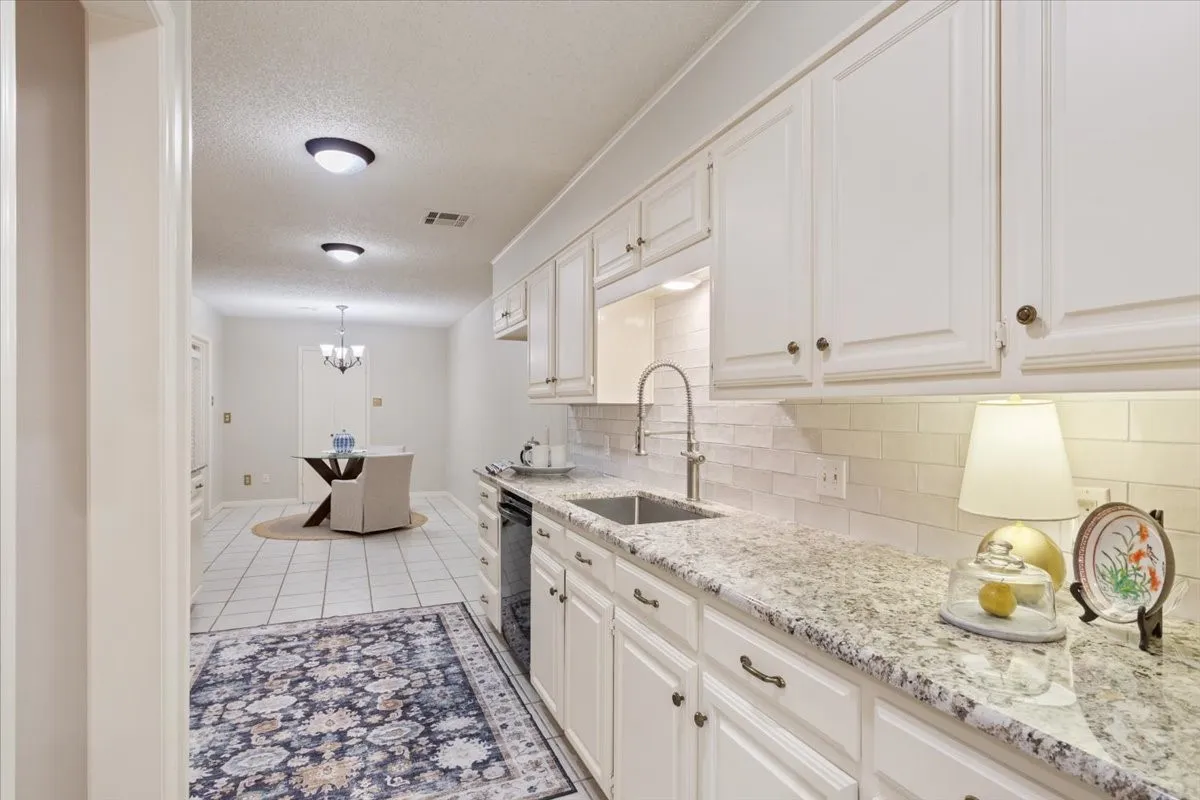 Elegant galley kitchen featuring crisp white cabinetry with hardware accents, granite countertops, a tile backsplash, and a pull-down faucet over the sink