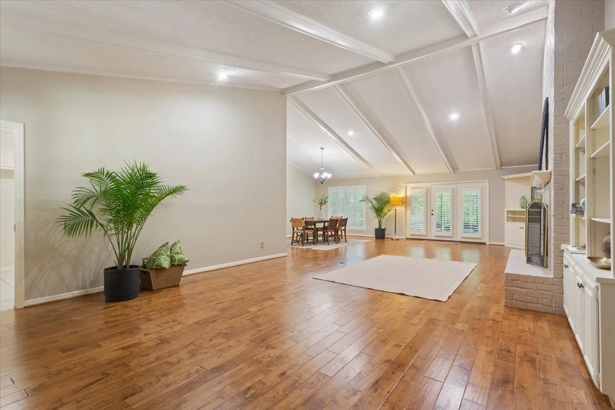 Spacious open-concept living area featuring coffered ceiling with recessed lighting, hardwood flooring throughout, and a custom built-in cabinetry wall with shelving and fireplace