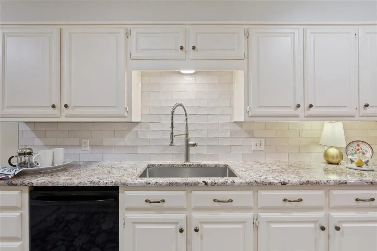 White shaker-style cabinetry, stainless steel sink, pull-down faucet, light-toned countertop, and subway tile backsplash