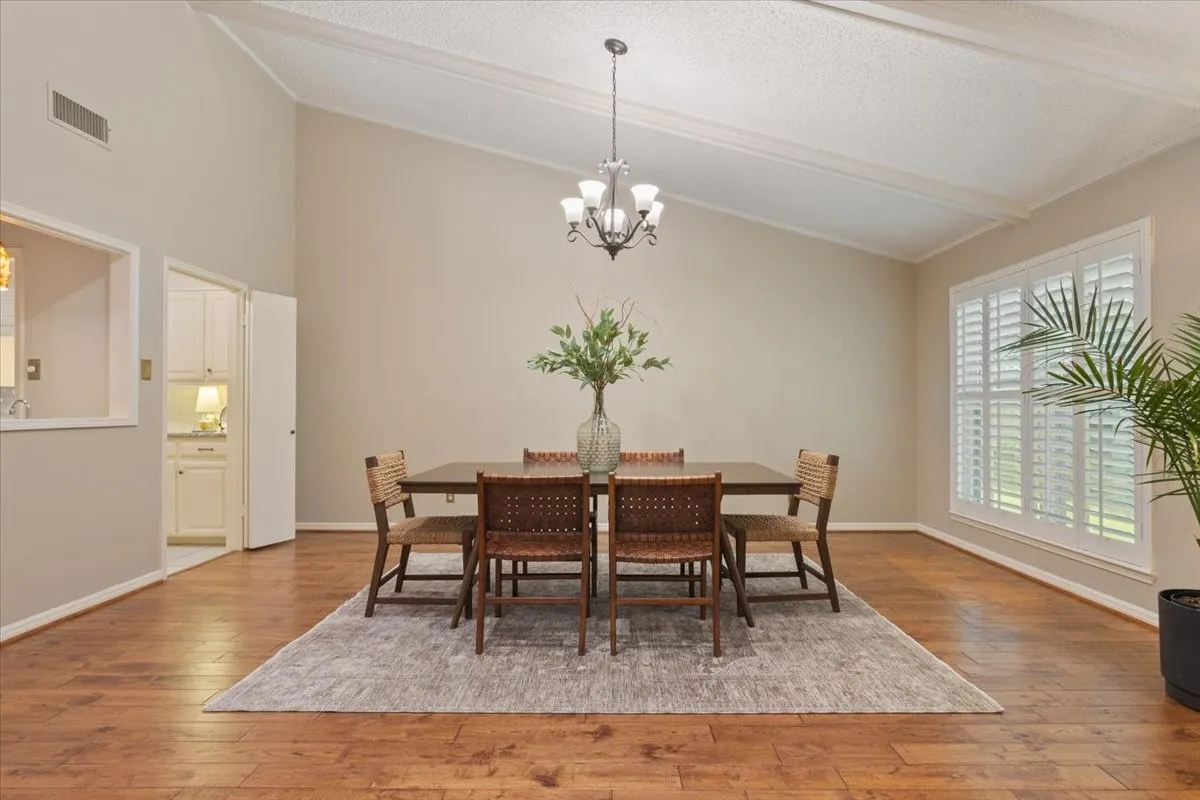Elegant dining room showcasing gleaming wood-finish flooring, abundant natural light from shuttered windows, and a pendant light fixture suspended from a coffered ceiling