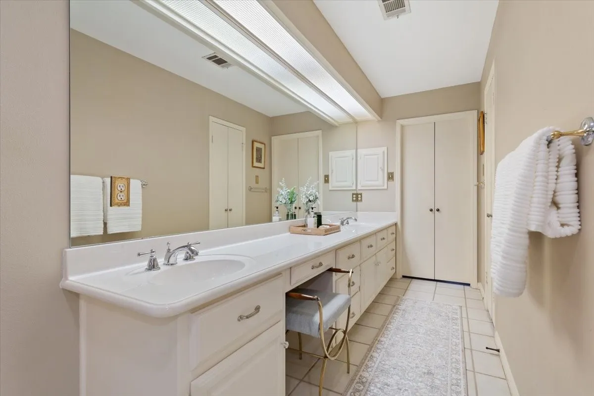 Spa-inspired primary bathroom featuring an extended dual-sink vanity with ample storage, polished chrome fixtures, and a frameless mirror