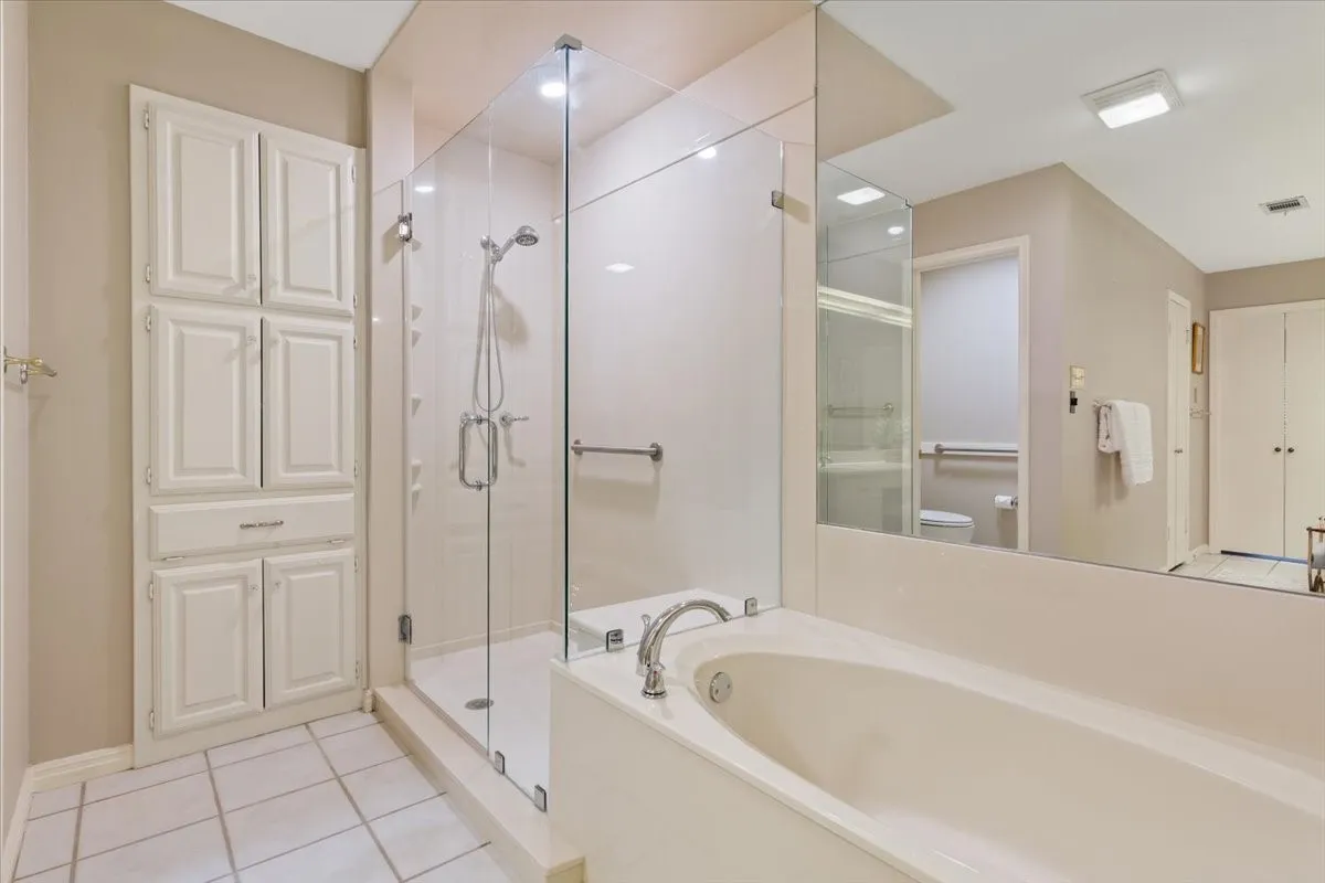 Spa-inspired primary bathroom featuring an updated frameless glass-enclosed shower with chrome fixtures, dual vanity countertop and integrated sink, large soaking tub, and abundant light from recessed ceiling fixtures