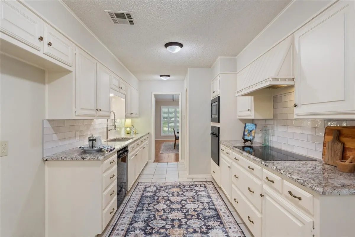 Galley kitchen featuring extensive white cabinetry, light-toned countertops, subway tile backsplash, and stainless steel sink