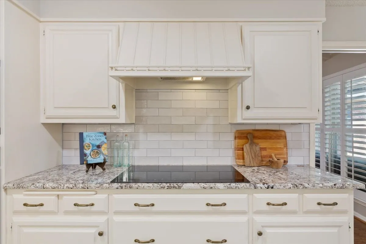White cabinetry with decorative pulls, integrated cooktop, subway tile backsplash, and light-toned countertops