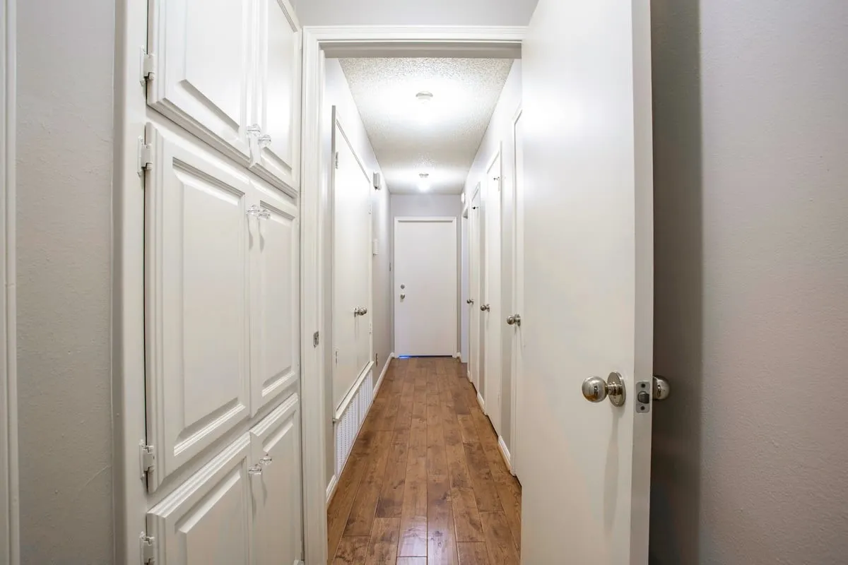 Ample storage space available in the hallway- a coat closet, two linen closets and linen cabinets available in the hallway with recessed lighting illuminating the wood flooring