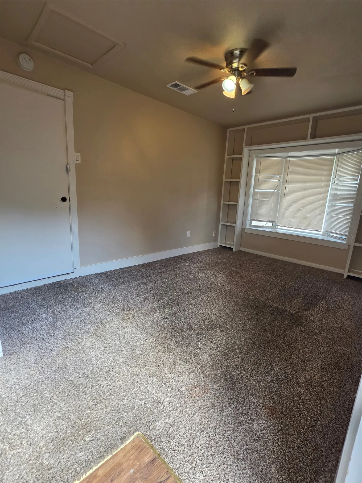 Recessed bay window with integrated shelving, ceiling fan with light fixture, and neutral-toned wall paint