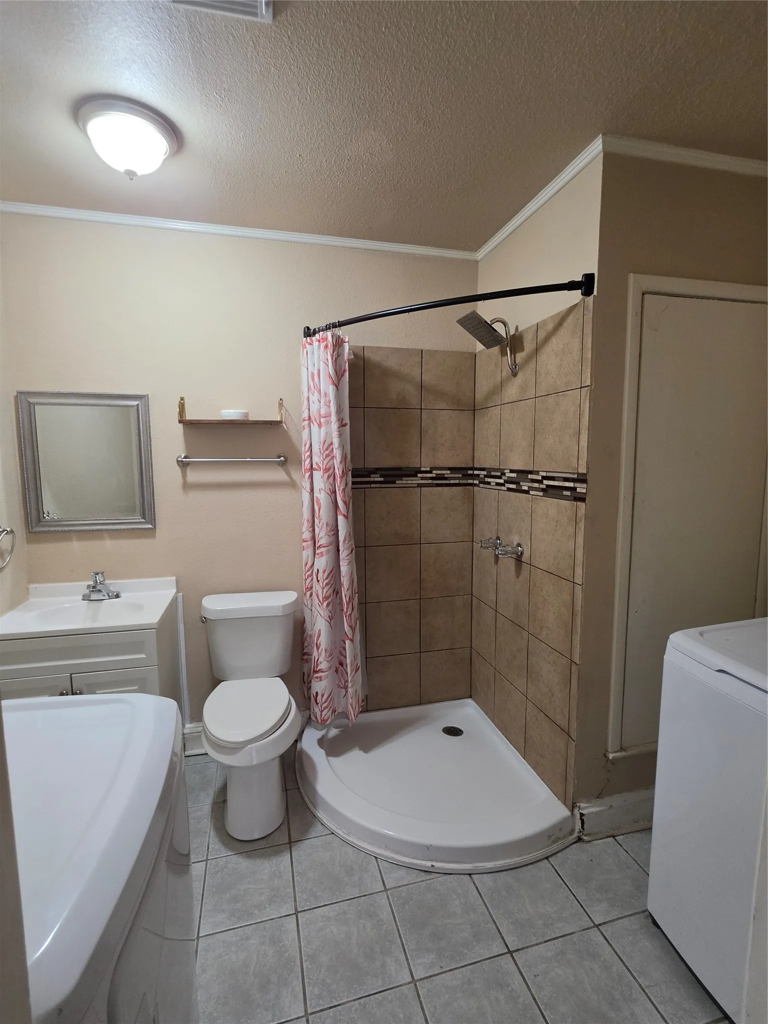Bathroom featuring a corner shower with tiled walls and decorative accent band, a single vanity with a basin sink, a toilet, and gray tiled flooring