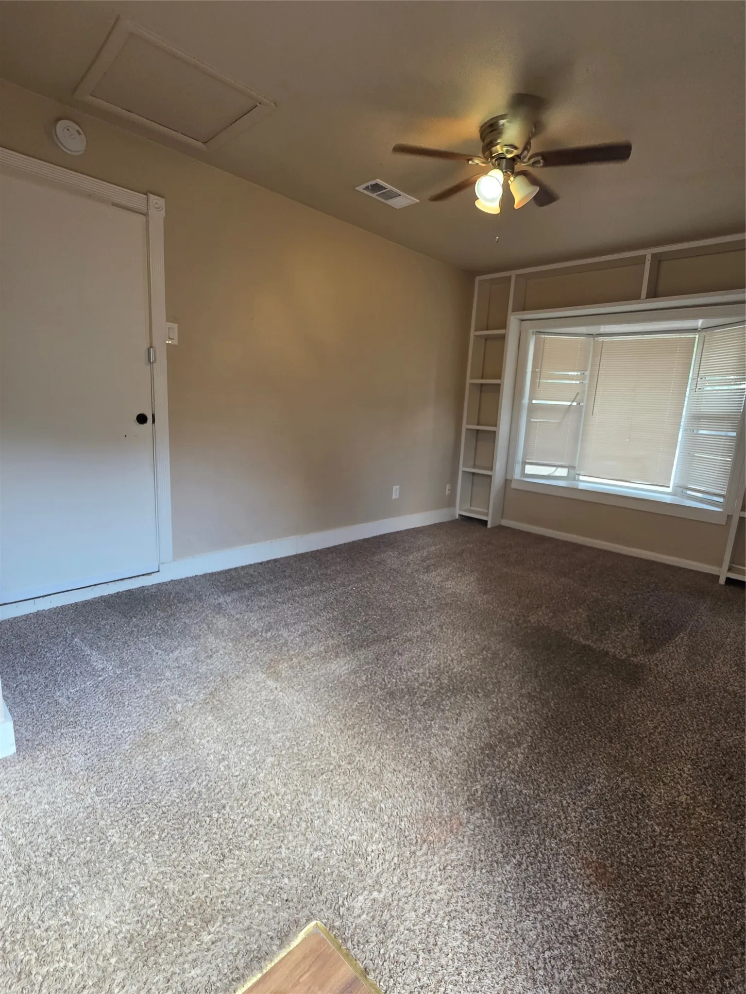 Textured carpeting, ceiling fan with integrated lighting, bay window, and built-in shelving