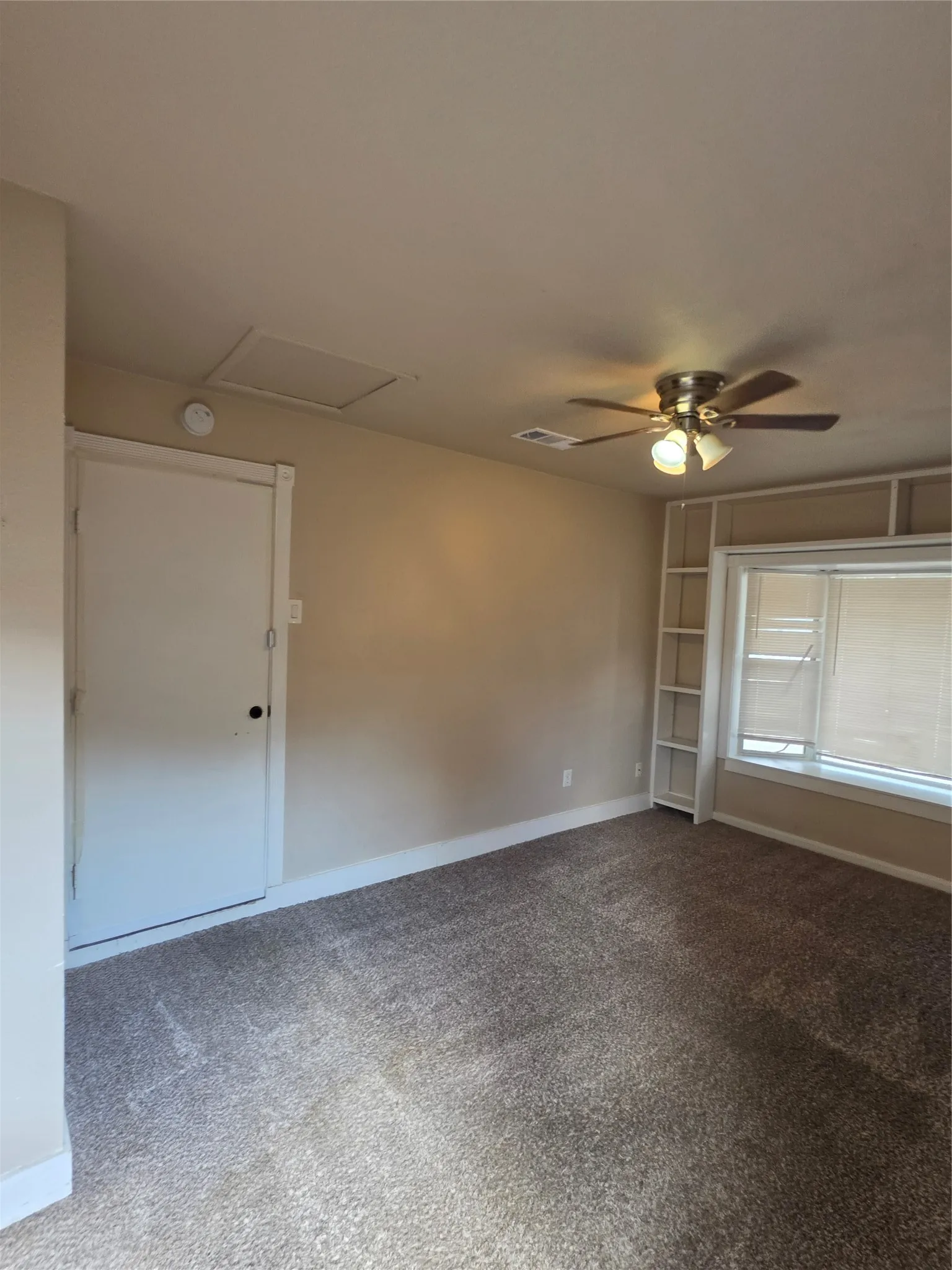 Wall-to-wall carpeting, ceiling fan with integrated lighting, built-in shelving, and a prominent window