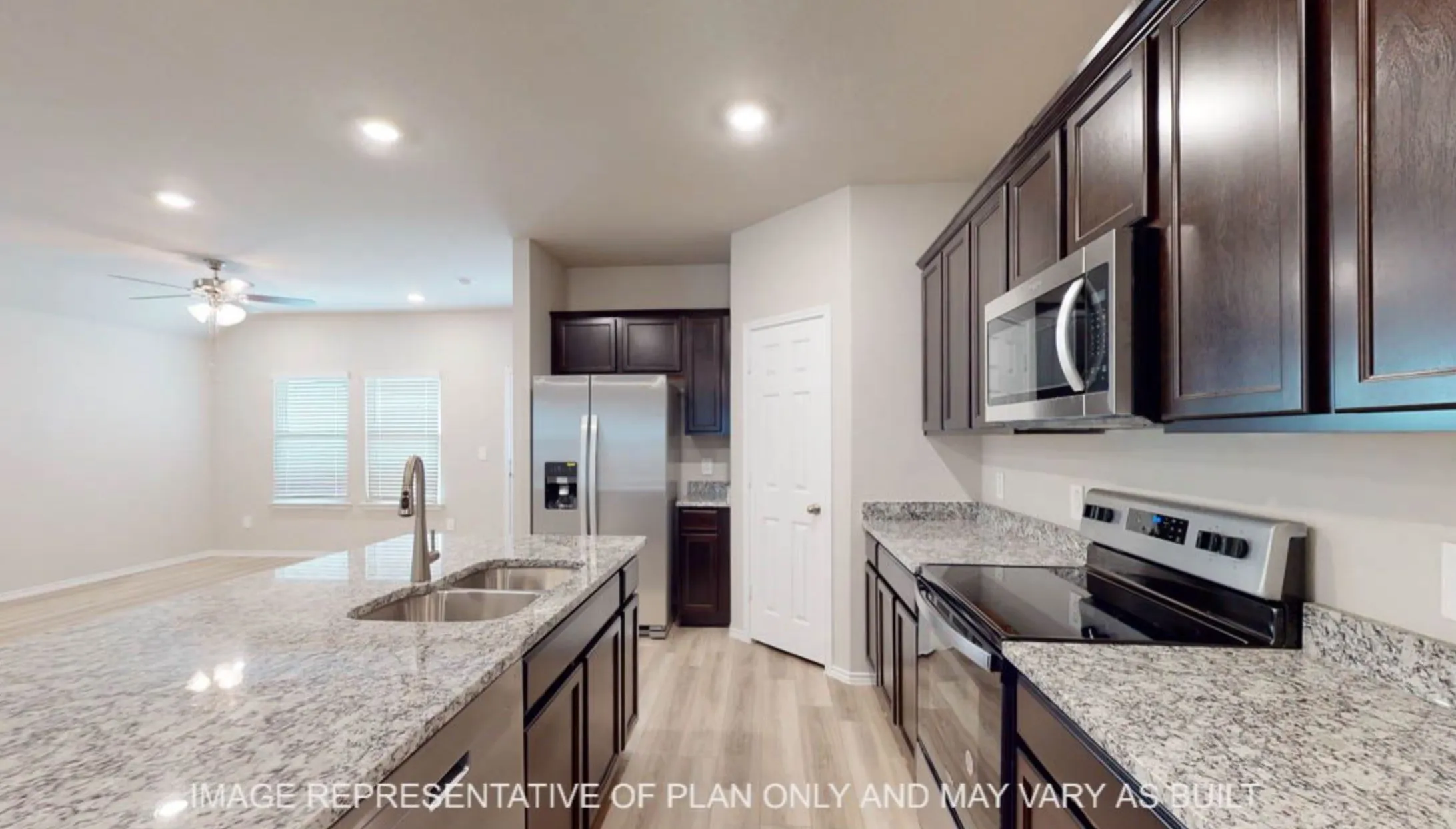 Kitchen featuring dark wood cabinetry, stainless steel appliances, light granite countertops, and wood-finish flooring