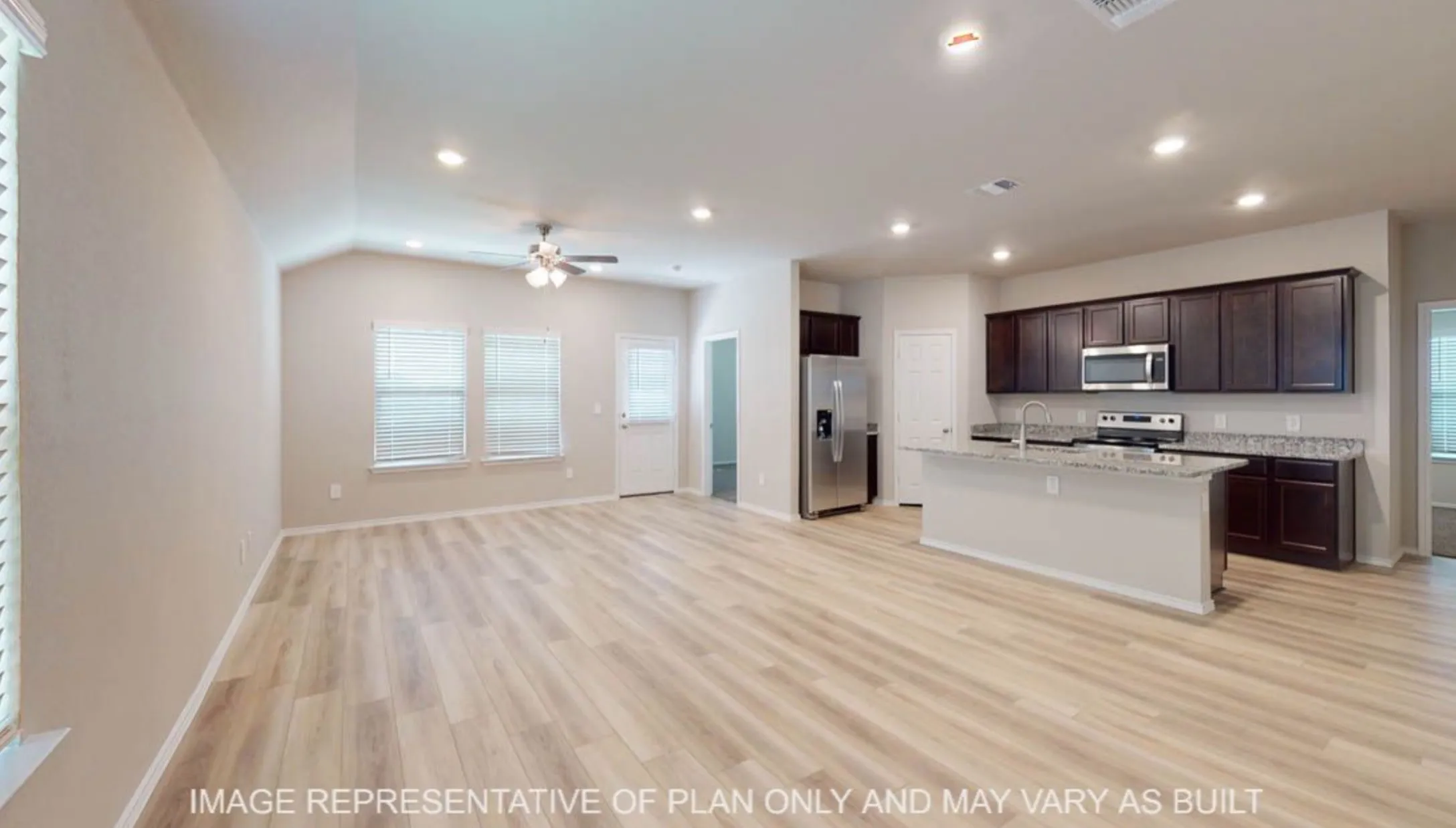 Vaulted ceiling, recessed lighting, wood-finish flooring, kitchen island with integrated sink, stainless steel appliances, dark wood-finish cabinetry, light-toned countertops