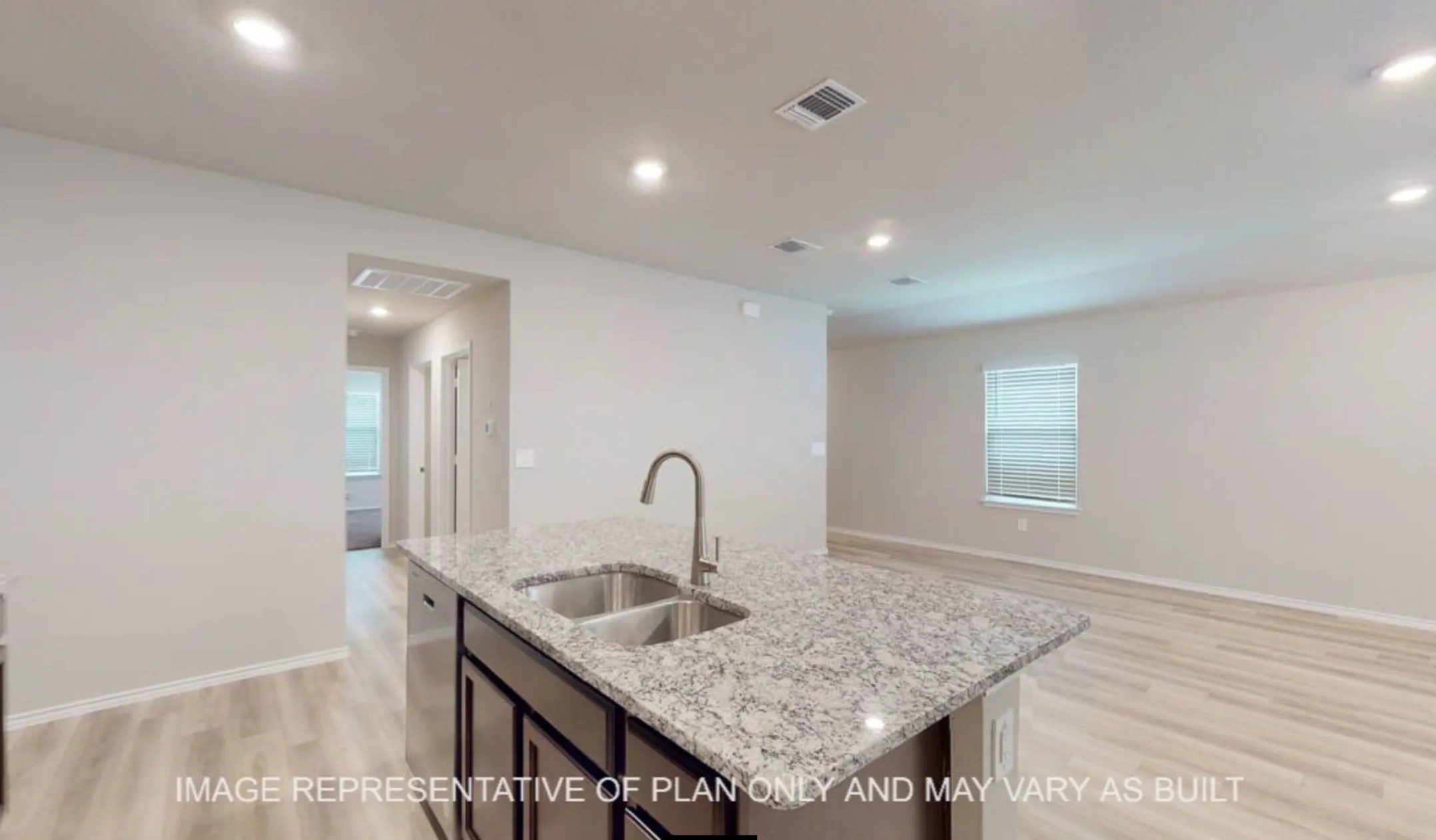 Modern kitchen and open living area featuring a dual-basin stainless steel sink, polished stone countertops, contemporary faucet with pull-down spray, light wood-finish flooring, recessed ceiling lighting, and abundant natural light from multiple windows