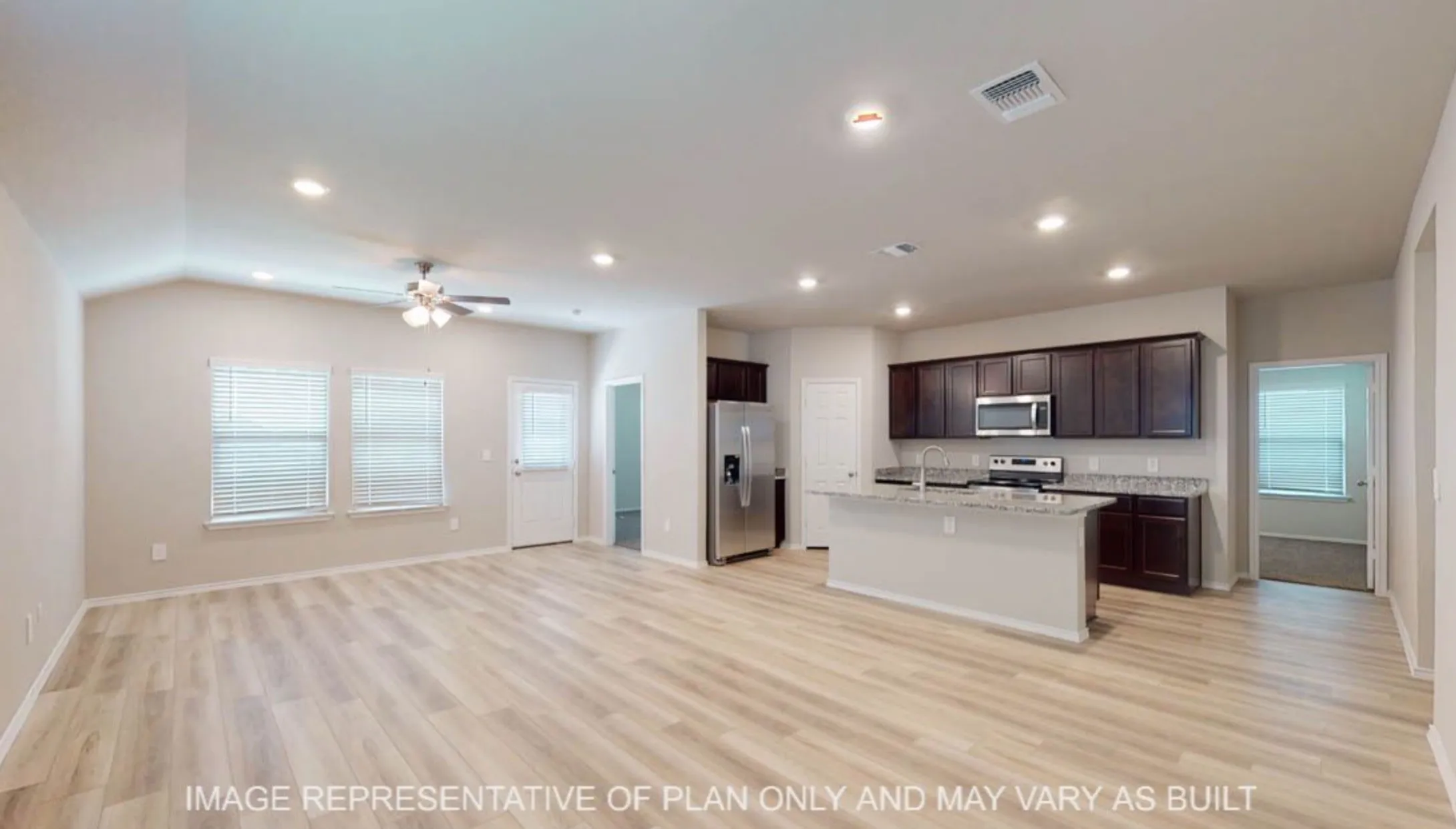 Spacious open-concept living area featuring wood-finish flooring, vaulted ceilings, and recessed lighting