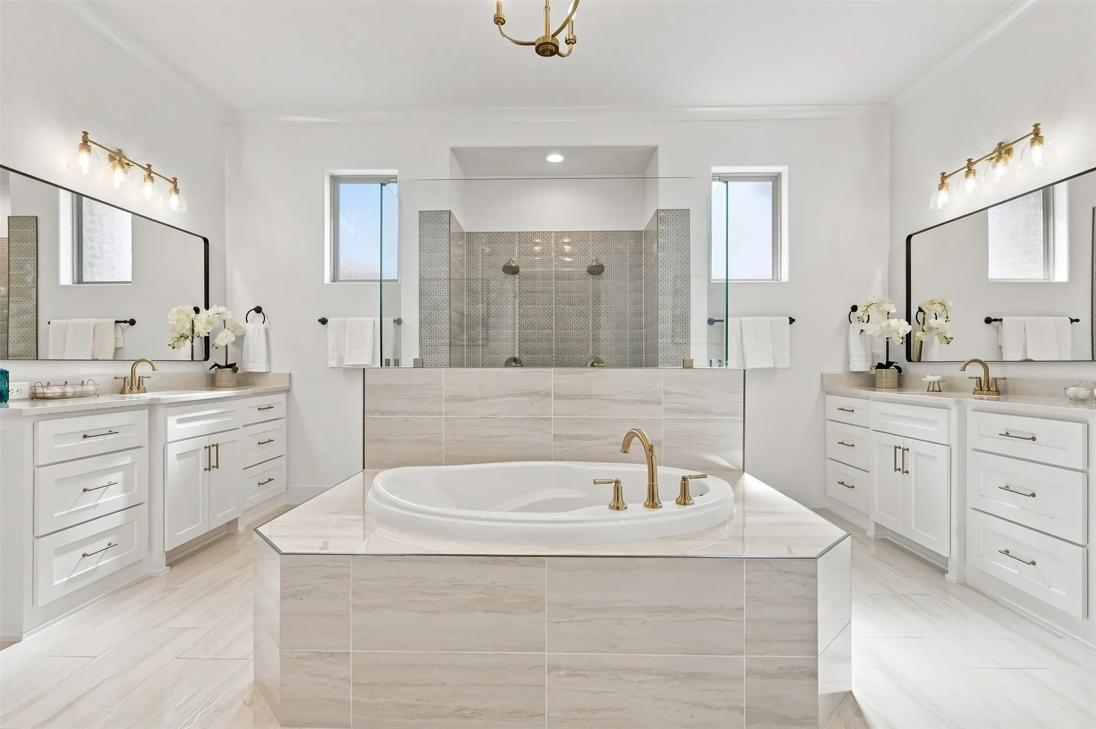 Spa-inspired primary bathroom featuring dual vanities with white cabinetry and brass hardware, quartz countertops, and integrated vessel sinks