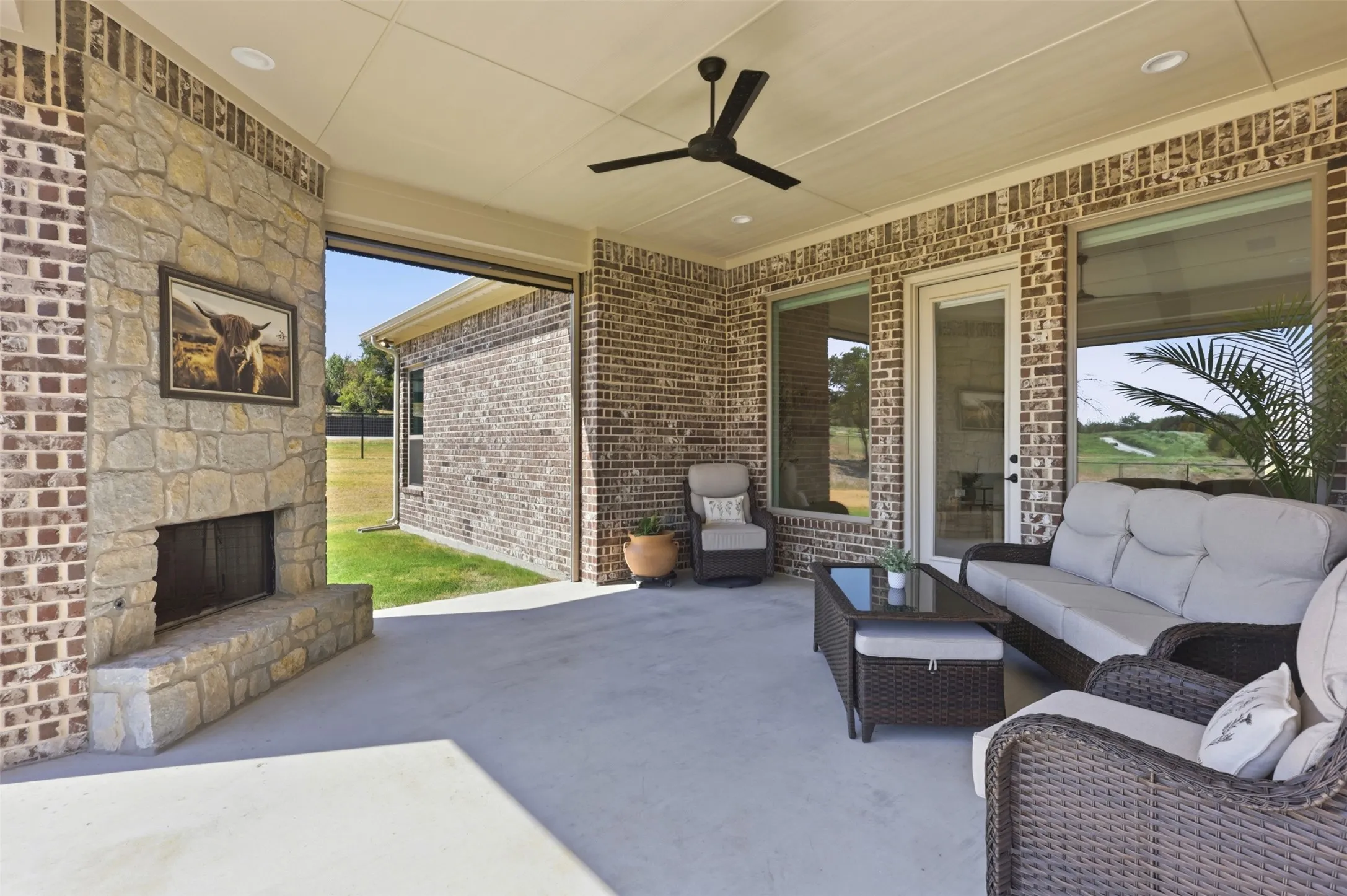 Covered patio featuring a stone fireplace, brick exterior walls, and a ceiling fan, and motorized screened in porch.