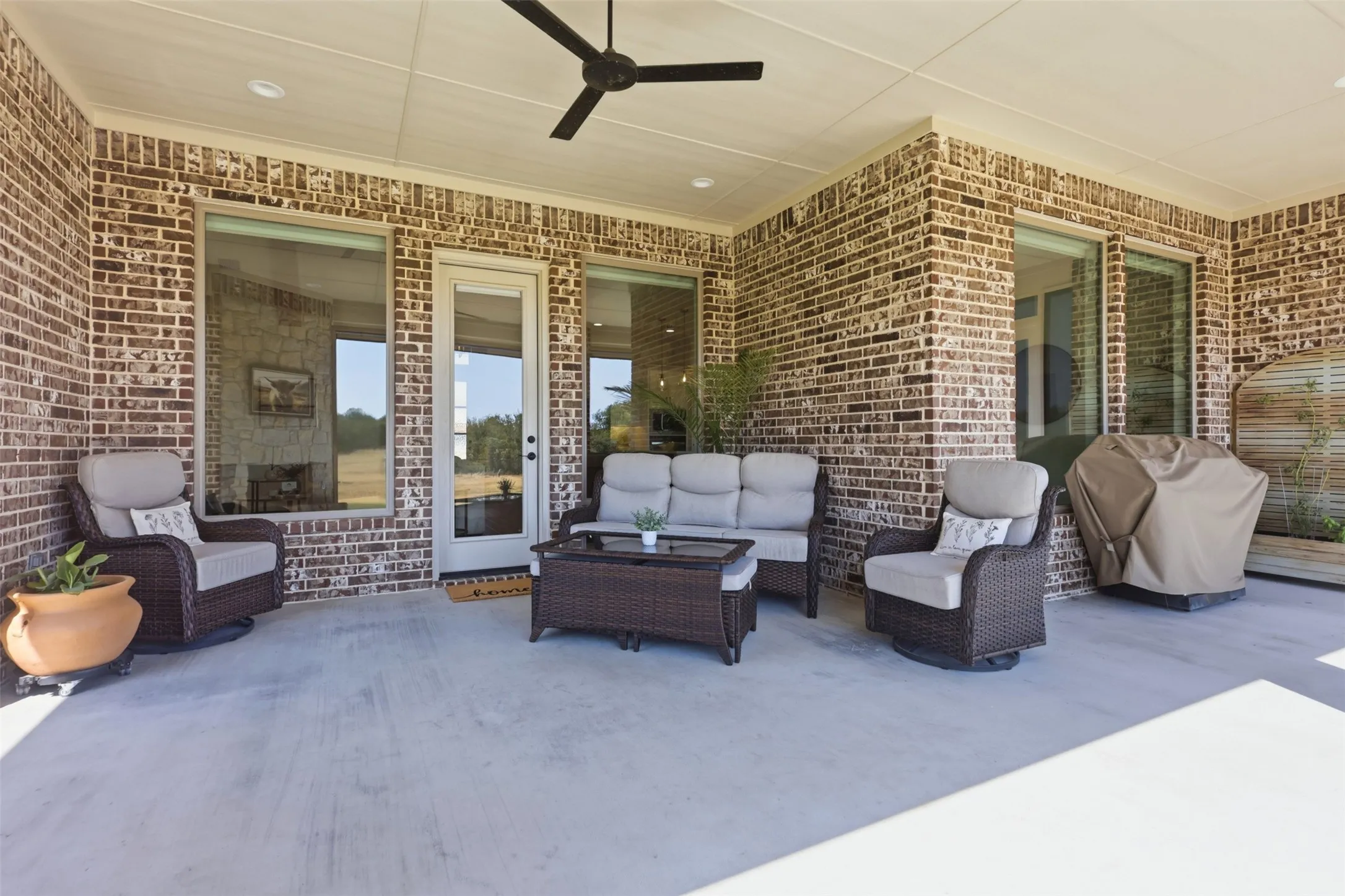 Covered patio featuring a ceiling fan, brick exterior, concrete flooring, and multiple glass-paned windows