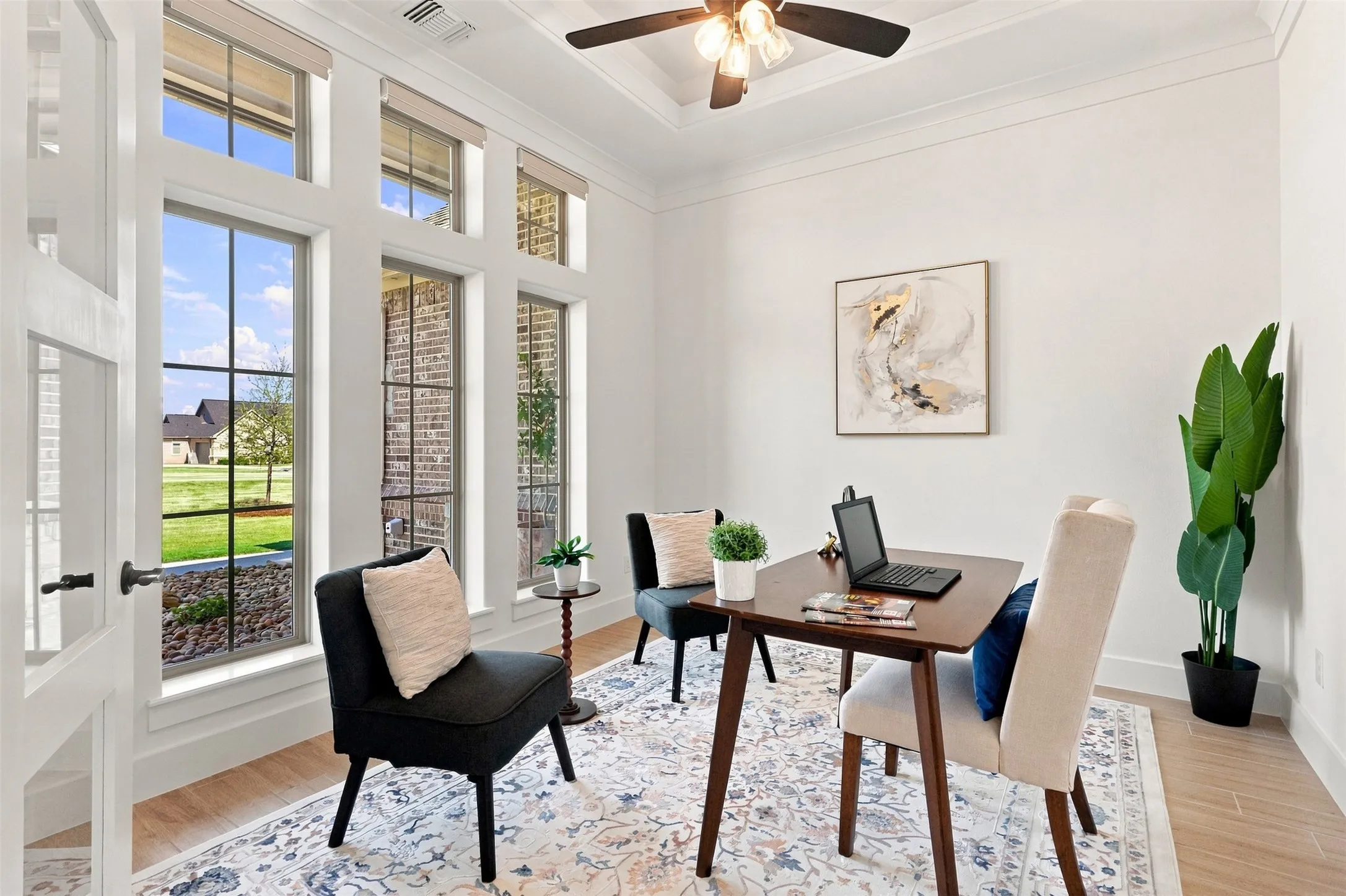 Tall windows with transoms, wood-finish flooring, a ceiling fan with integrated lighting, and a white paneled door with glass inserts, motorized blinds