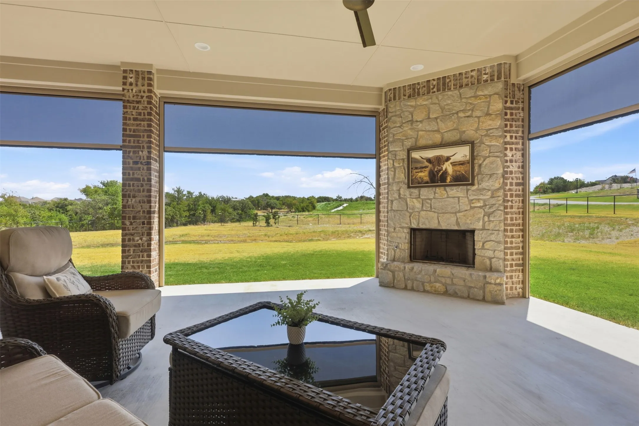 Covered patio with a stone and brick fireplace, large windows, ceiling fan, and recessed lighting and motorized screened in porch