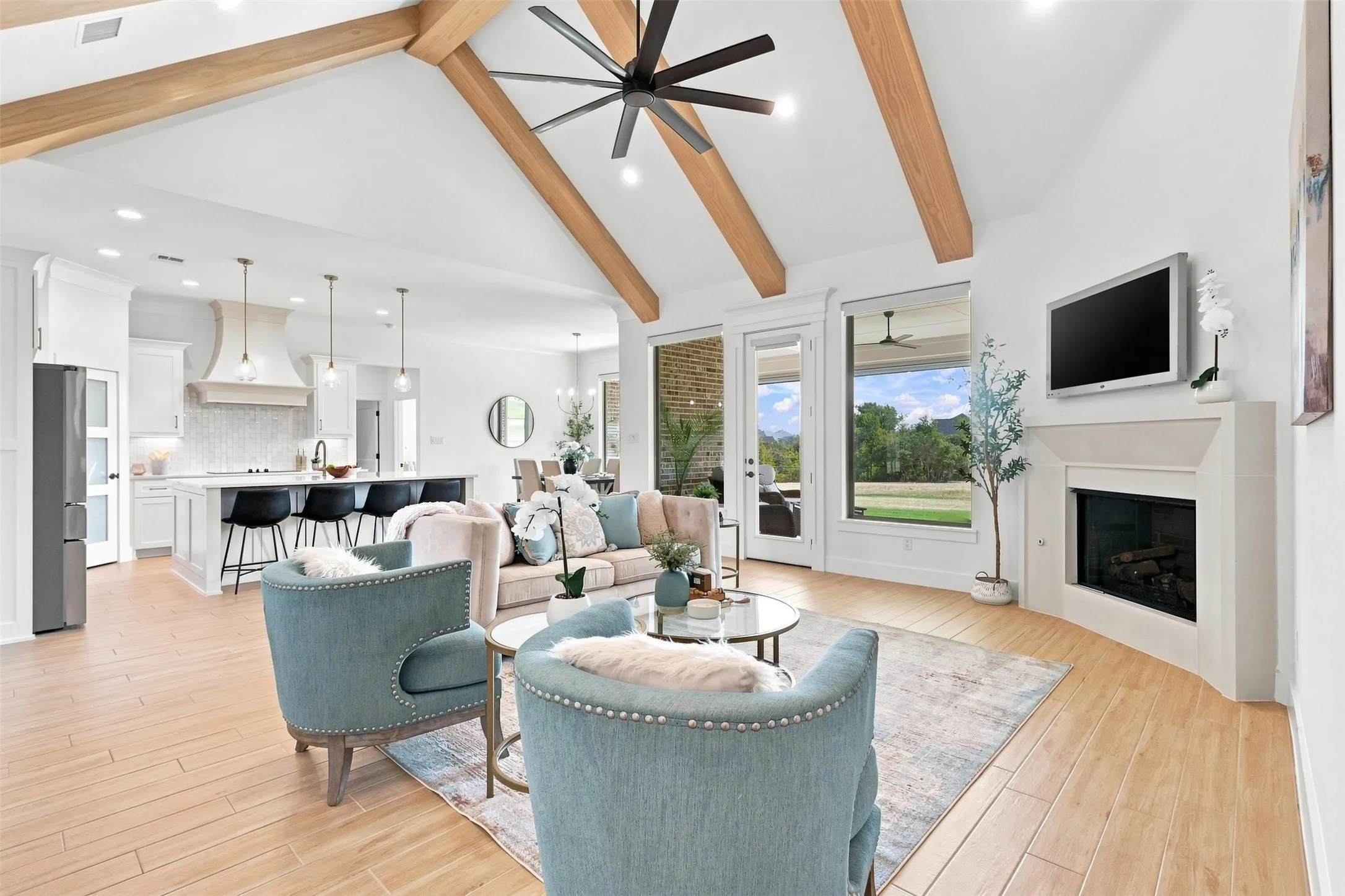 Vaulted ceiling with exposed wood beams, wood-finish flooring, built-in gas fireplace, and expansive windows with motorized blinds