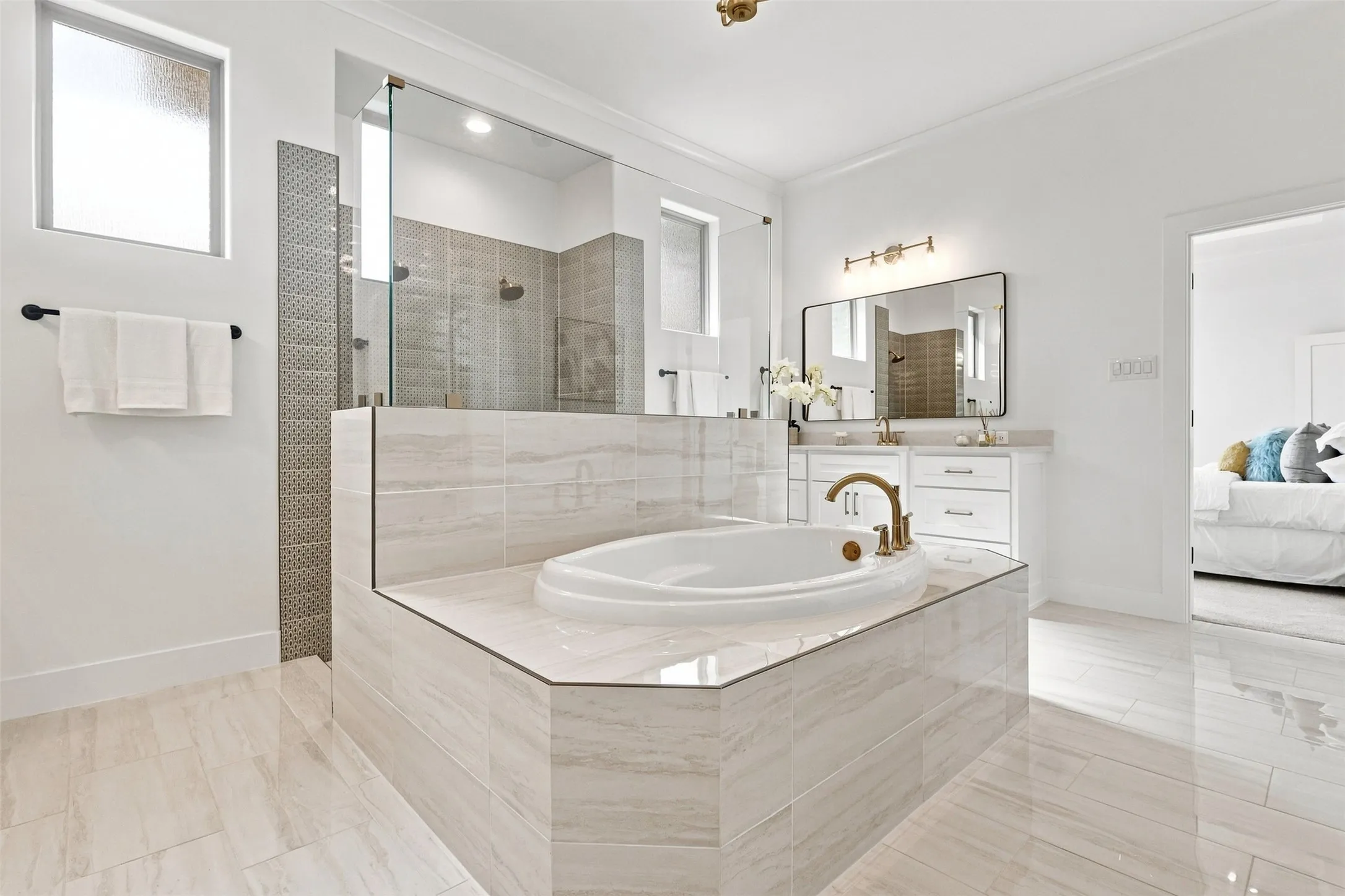 Built-in soaking tub with tiled surround, walk-in shower with glass enclosure and tiled walls, dual vanity with undermount sinks, and polished tile flooring