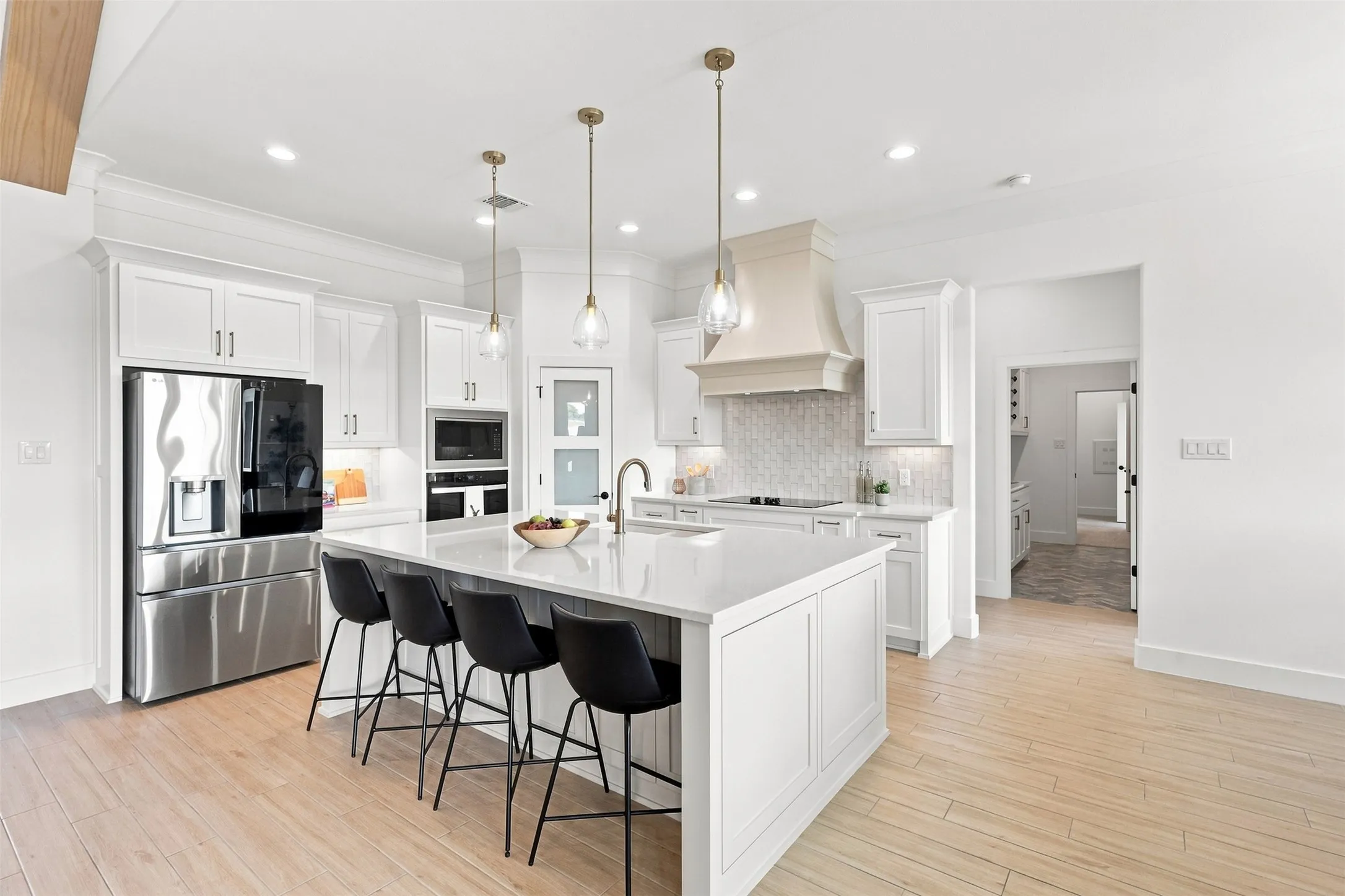 Spacious kitchen with a large central island, white cabinetry, integrated stainless steel appliances, a decorative range hood, and wood-finish flooring