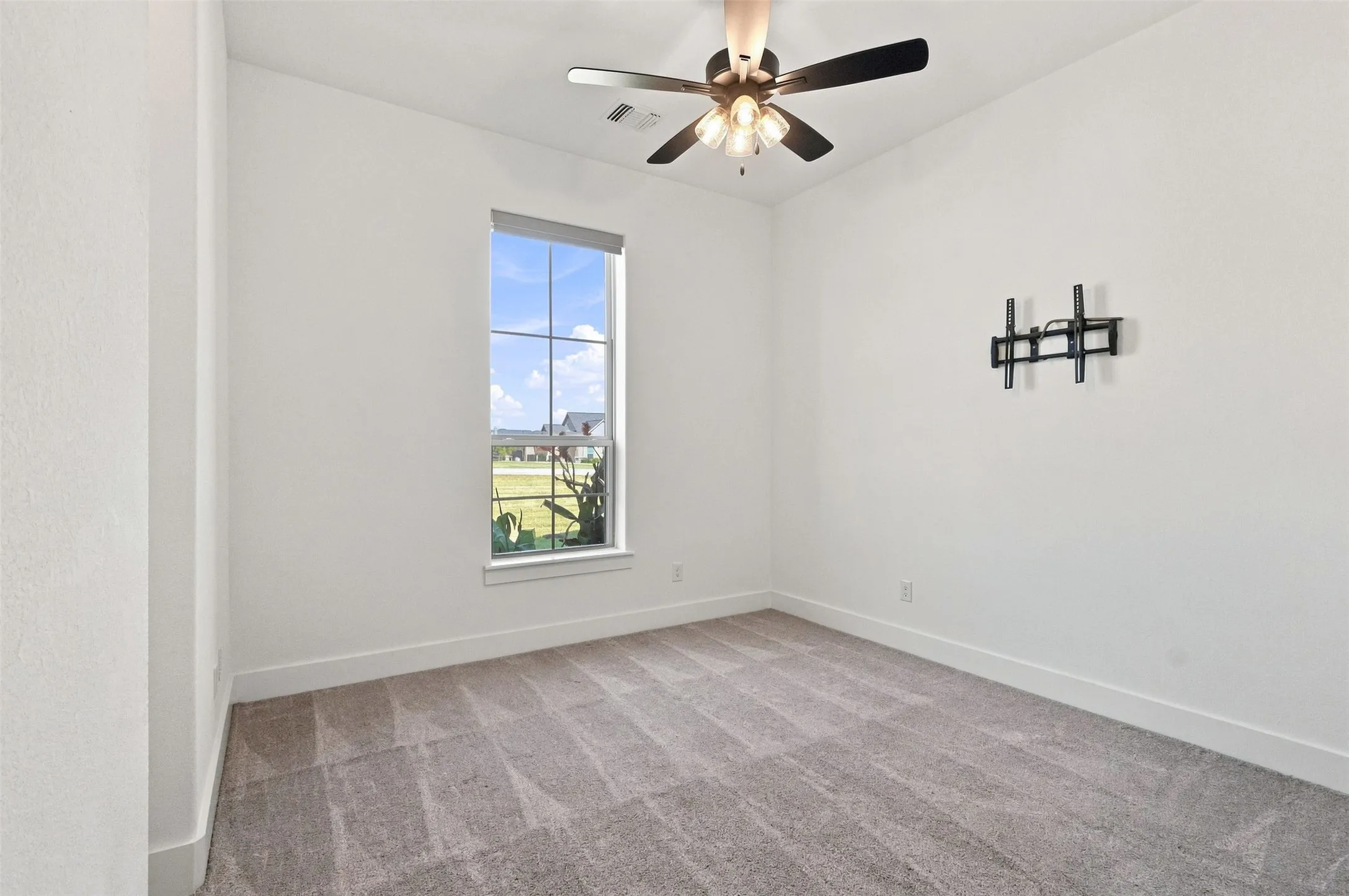 Carpeted room with a ceiling fan, a window with motorized blinds, and a wall-mounted bracket
