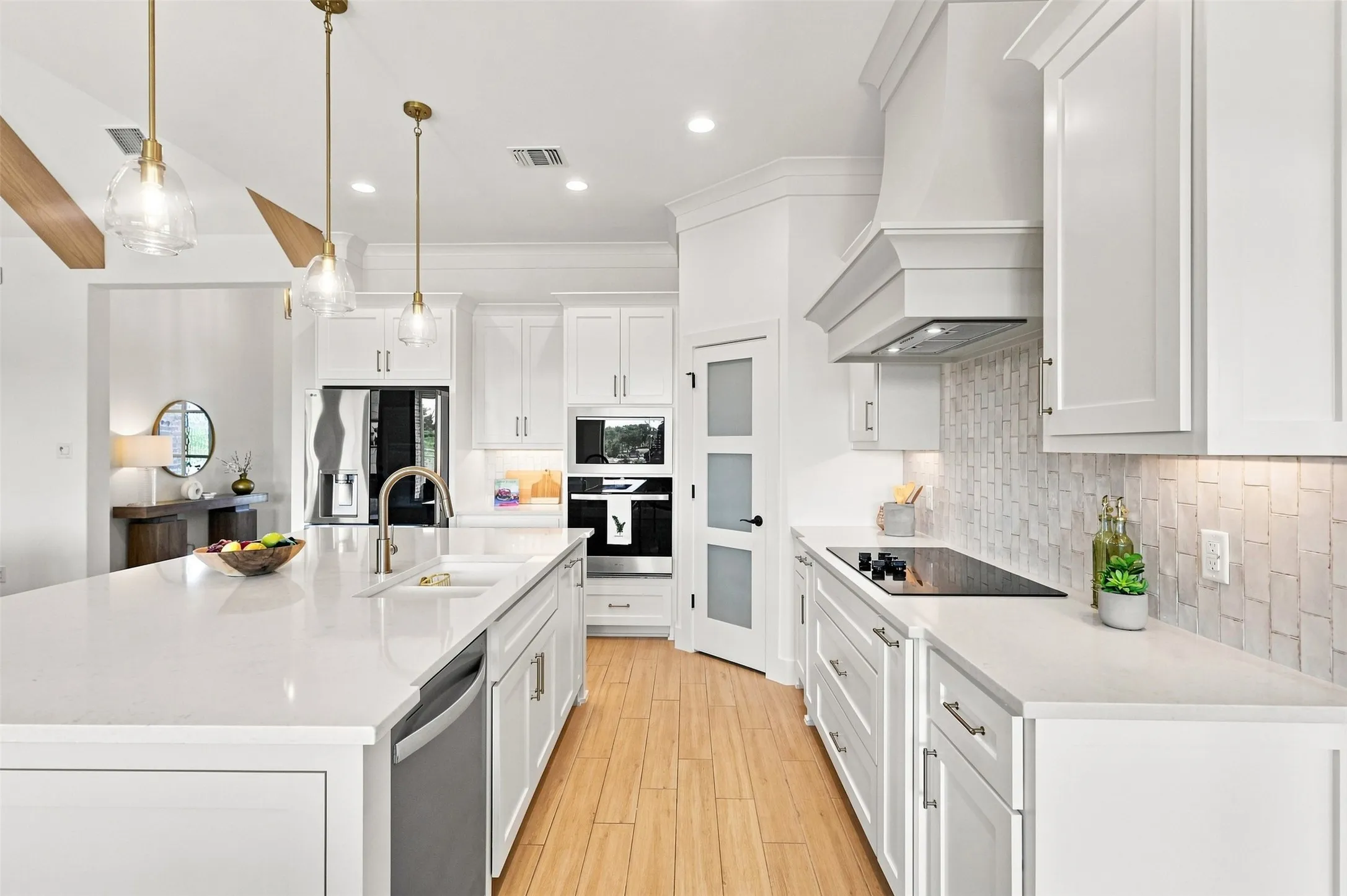 Kitchen featuring light wood-finish flooring, white cabinetry, integrated stainless steel appliances, a spacious island with an undermount sink, and a tiled backsplash
