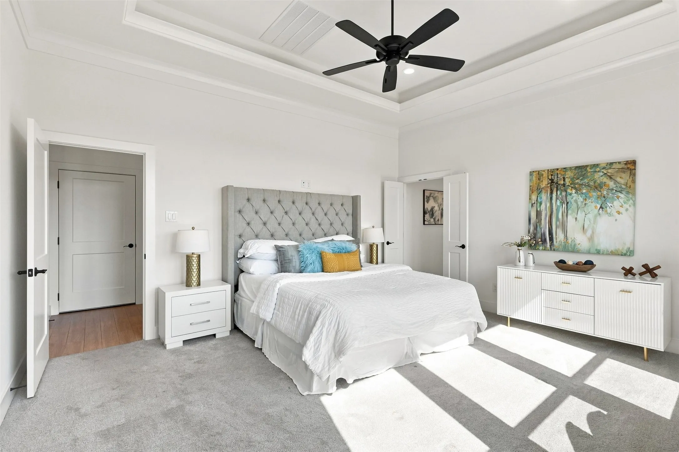 Recessed tray ceiling with a black ceiling fan, light gray carpeting, and white interior doors with black hardware