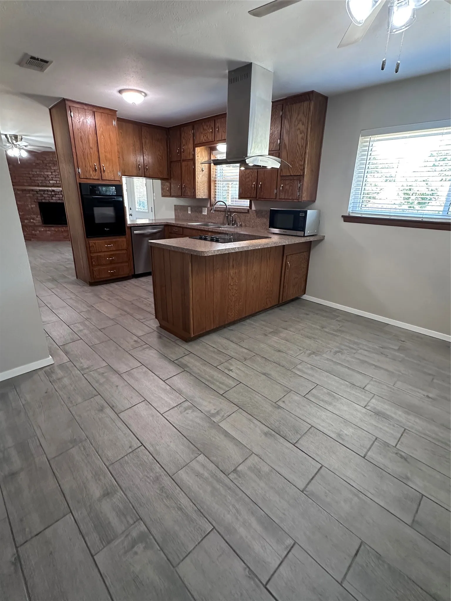 Kitchen featuring wood cabinetry, stainless steel range hood, integrated oven, and a built-in breakfast bar