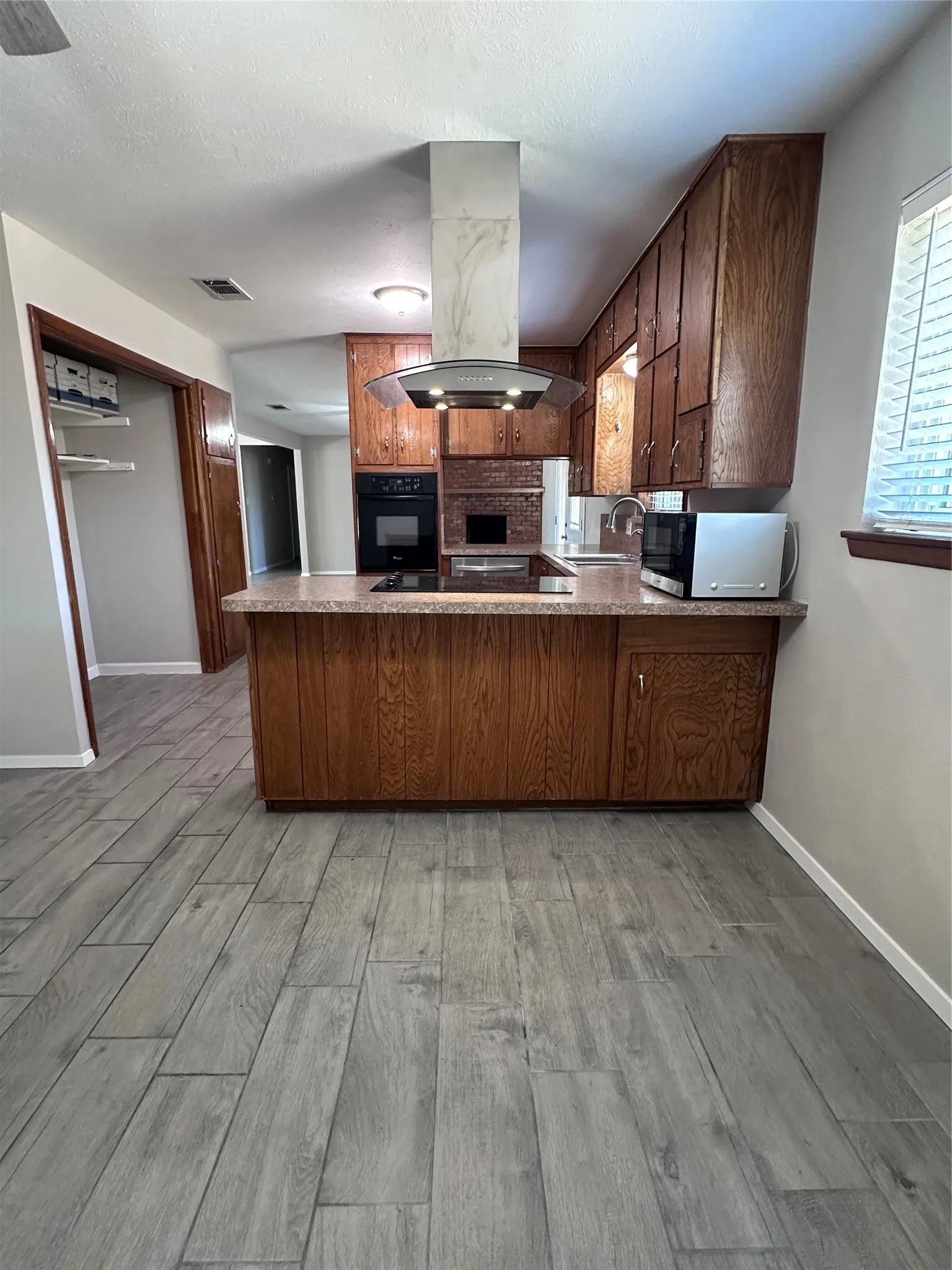 Kitchen featuring wood cabinetry, stone-finish countertops, built-in oven, and a modern range hood