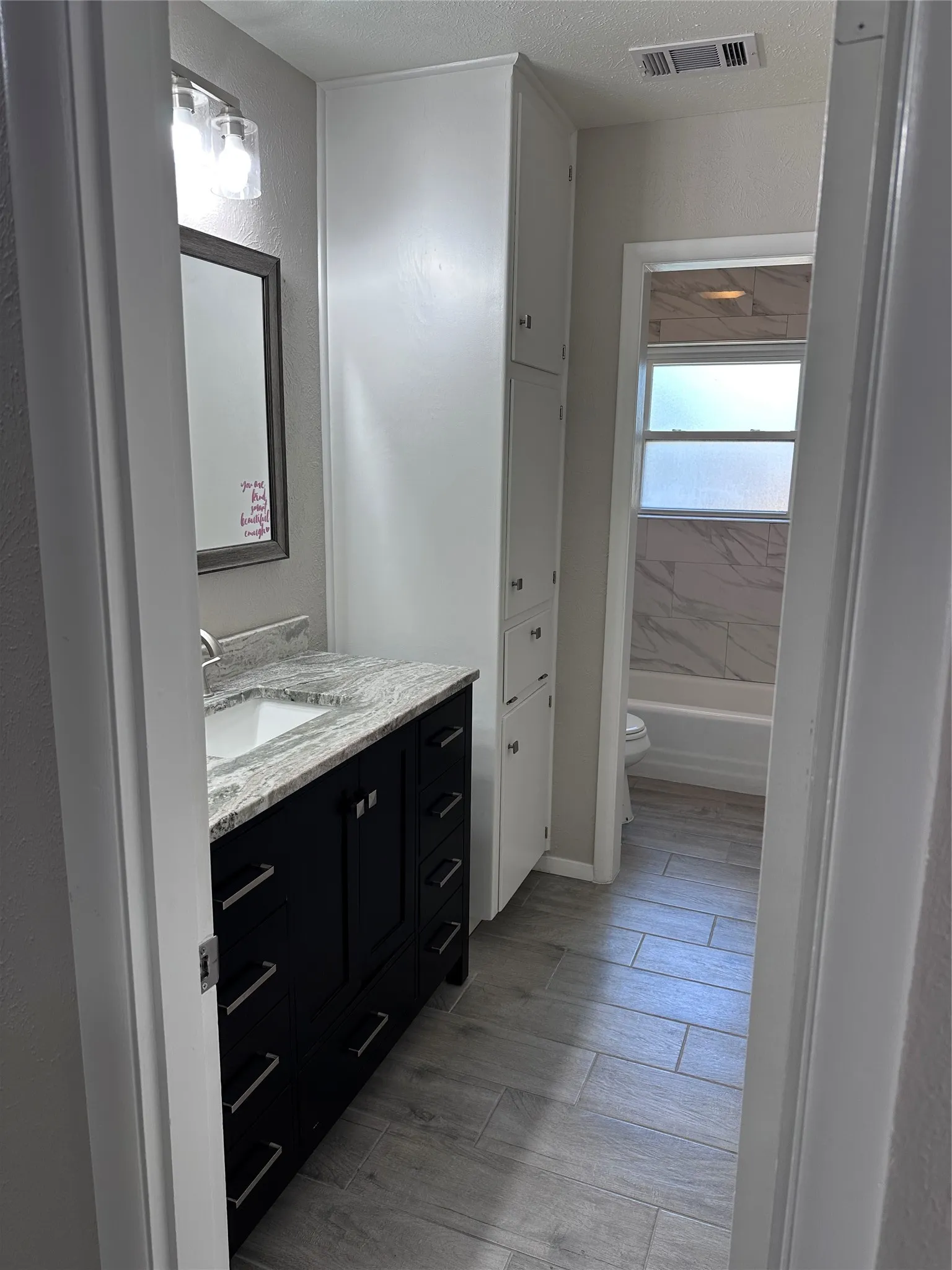 Bathroom featuring a dark vanity with a light-colored countertop, built-in storage cabinetry, and wood-finish tile flooring