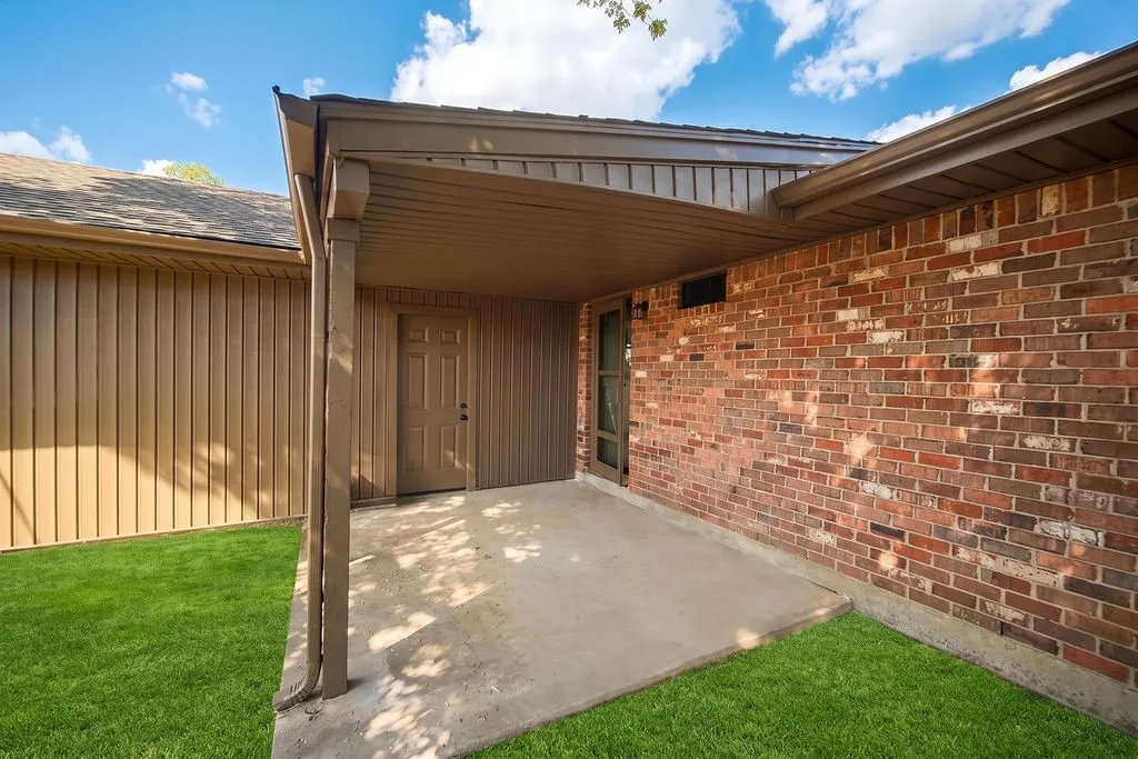Covered concrete patio with brick and vertical panel siding