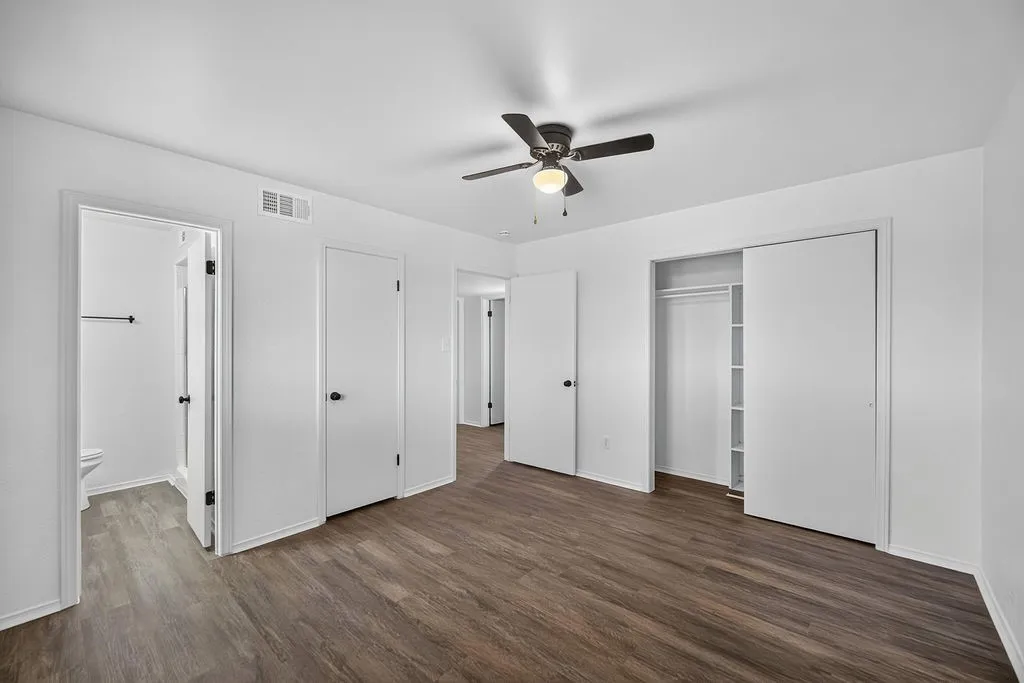 Wood-finish flooring, ceiling fan with integrated lighting, and multiple white panel doors