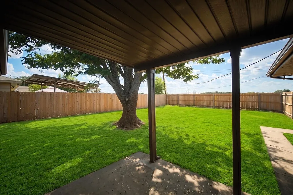Covered patio with concrete flooring, private wood fencing, and a manicured lawn