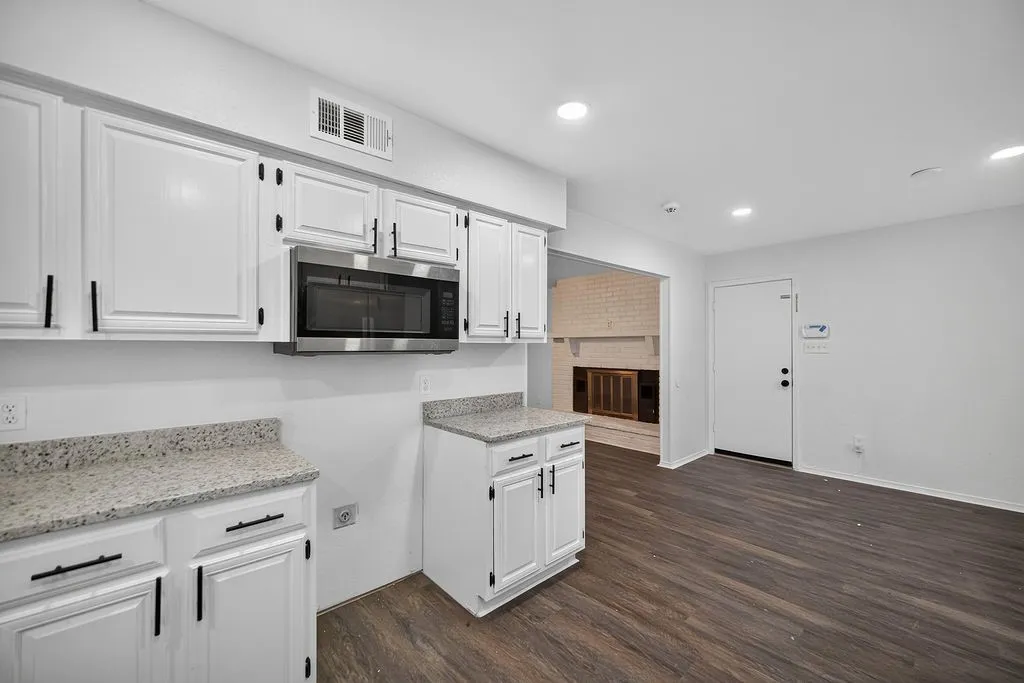 White cabinetry with matte black hardware, stainless steel microwave, stone-finish countertops, wood-finish flooring, recessed lighting