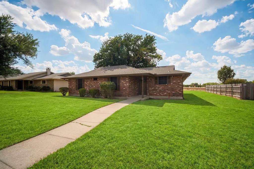 Brick exterior, established landscaping, concrete pathway, fenced perimeter, and expansive lawn