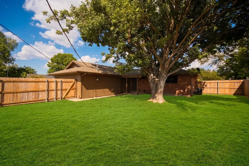 Expansive backyard featuring a manicured lawn, established tree, and wood privacy fencing