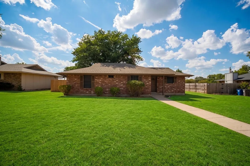Brick exterior, large front lawn, concrete walkway, mature landscaping, and an asphalt shingle roof