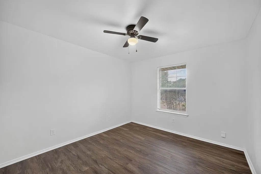 Wood-finish flooring, single window, white walls, and a ceiling fan with integrated lighting