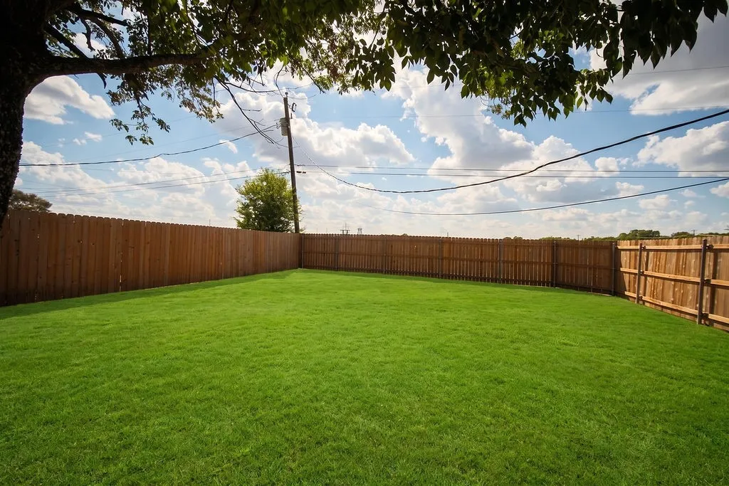 Expansive green lawn with a full privacy fence and mature tree