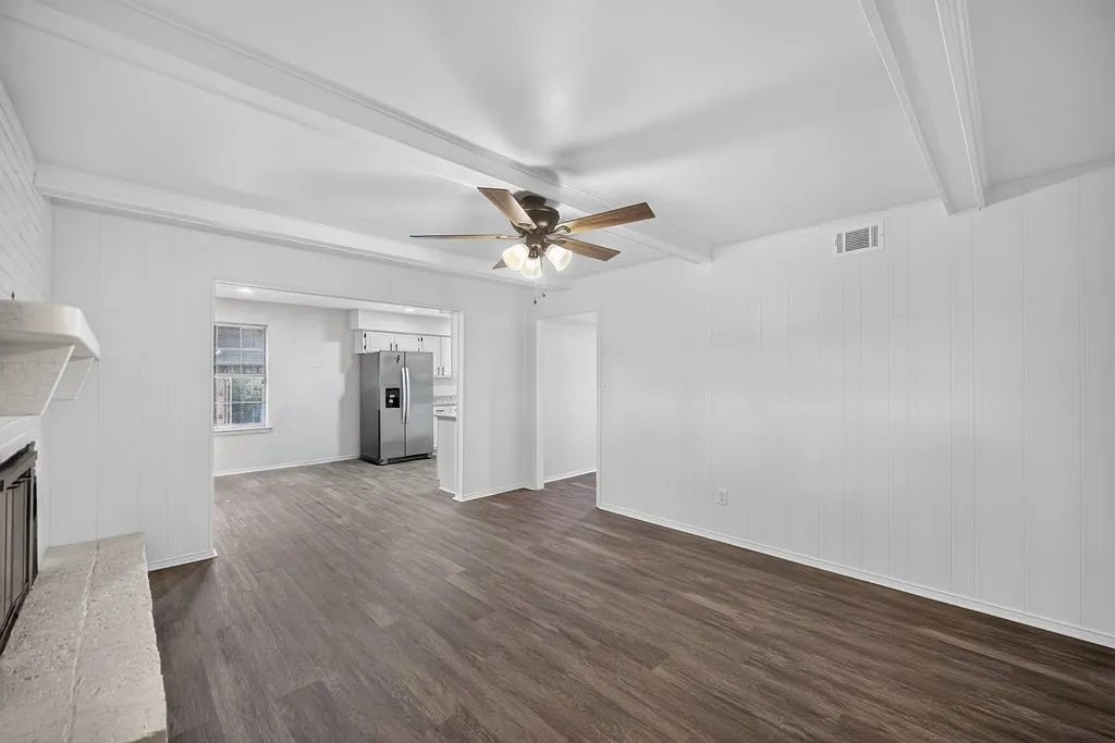 Wood-finish flooring, white paneling, exposed ceiling beams, and a fireplace with a stone hearth
