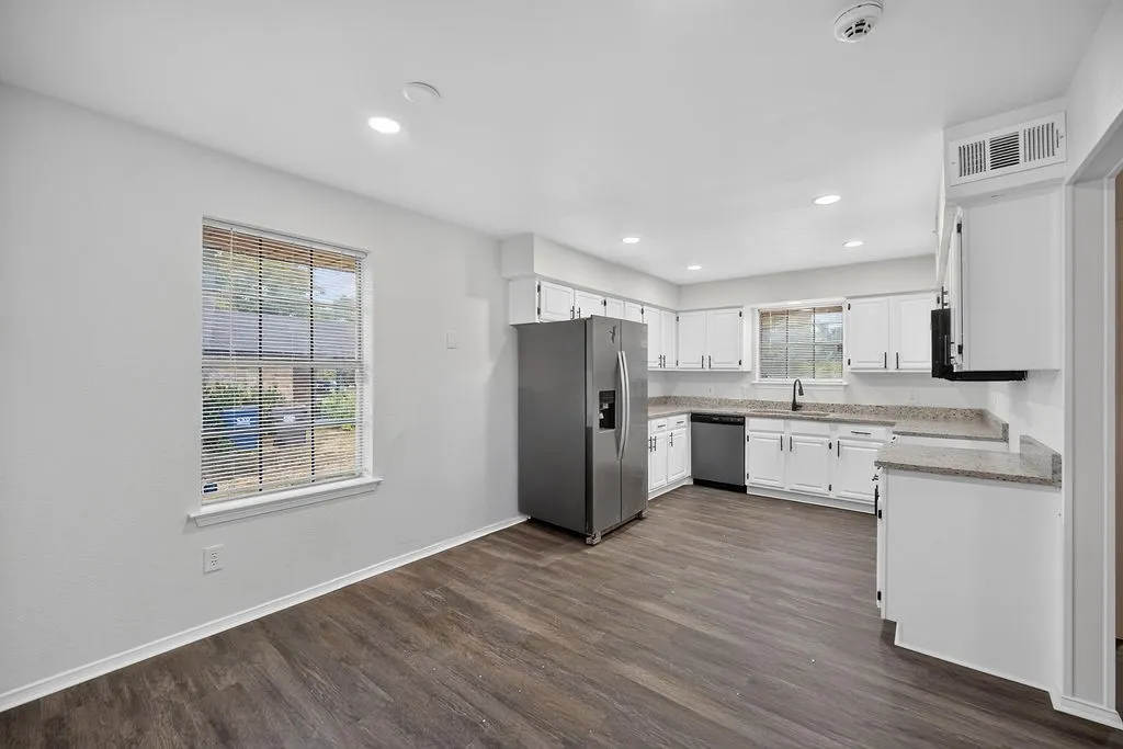 Kitchen with wood-finish flooring, white cabinetry, integrated stainless steel appliances, and recessed lighting
