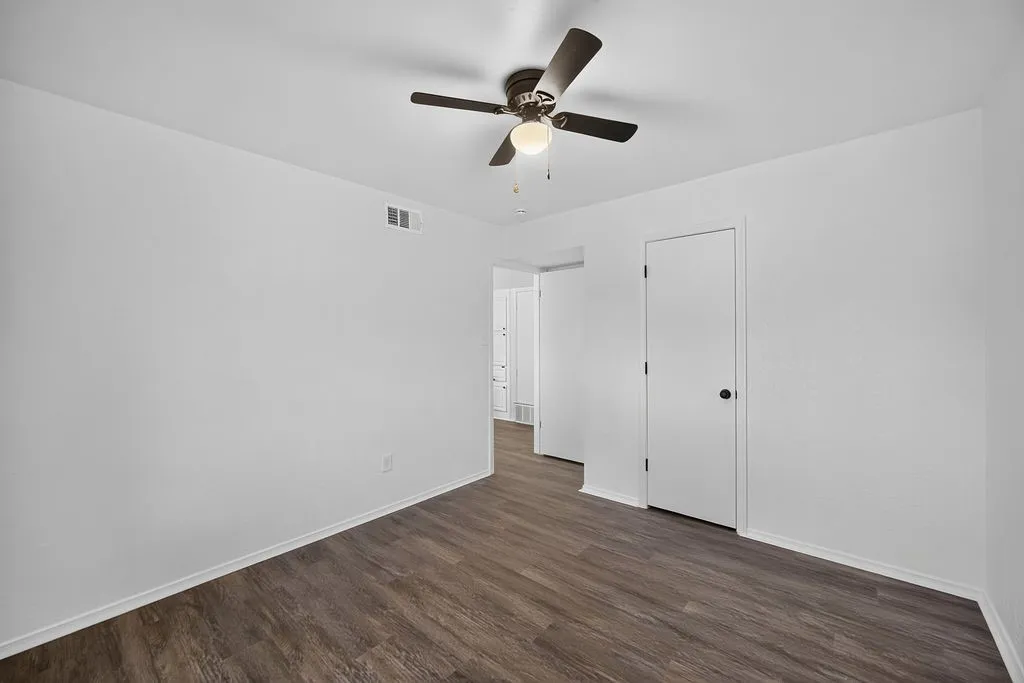 Wood-finish flooring, white walls, and a ceiling fan with integrated lighting