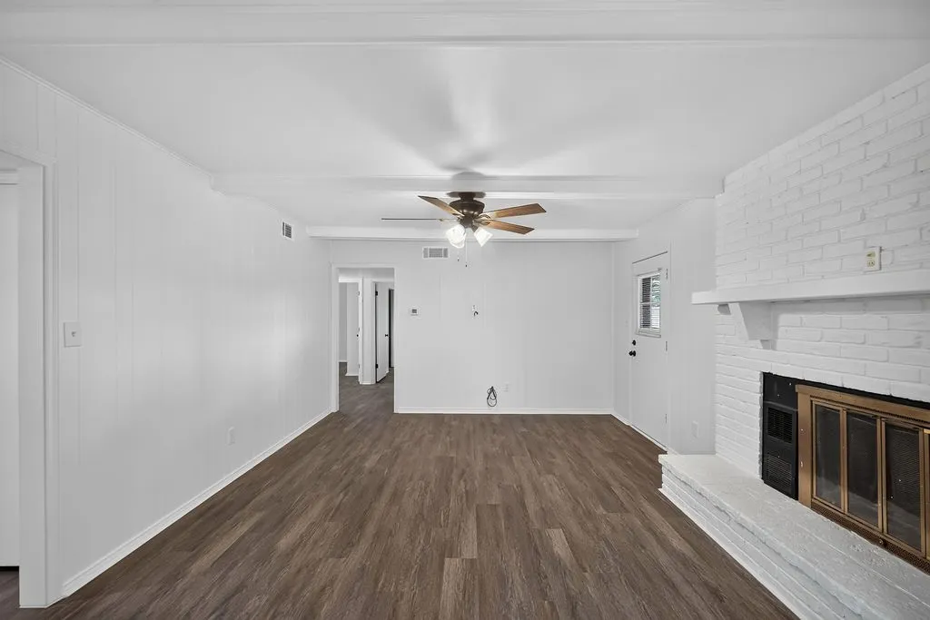Spacious living area featuring wood-finish flooring, a brick fireplace with a mantel, and a ceiling fan